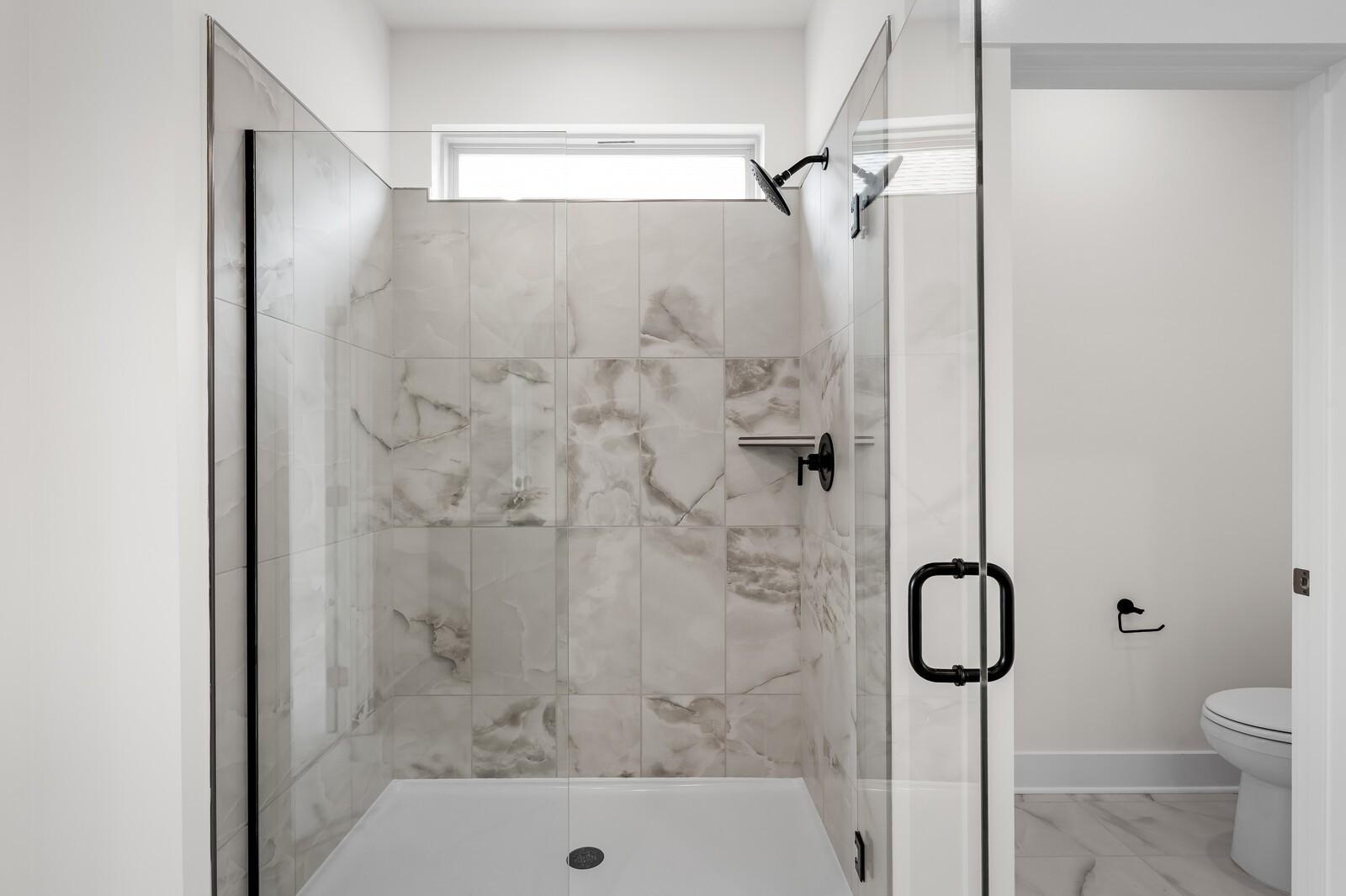 Modern walk-in shower with marble-look tile and glass door in a Davidson Homes floor plan at Woods Crossing, Gallatin.