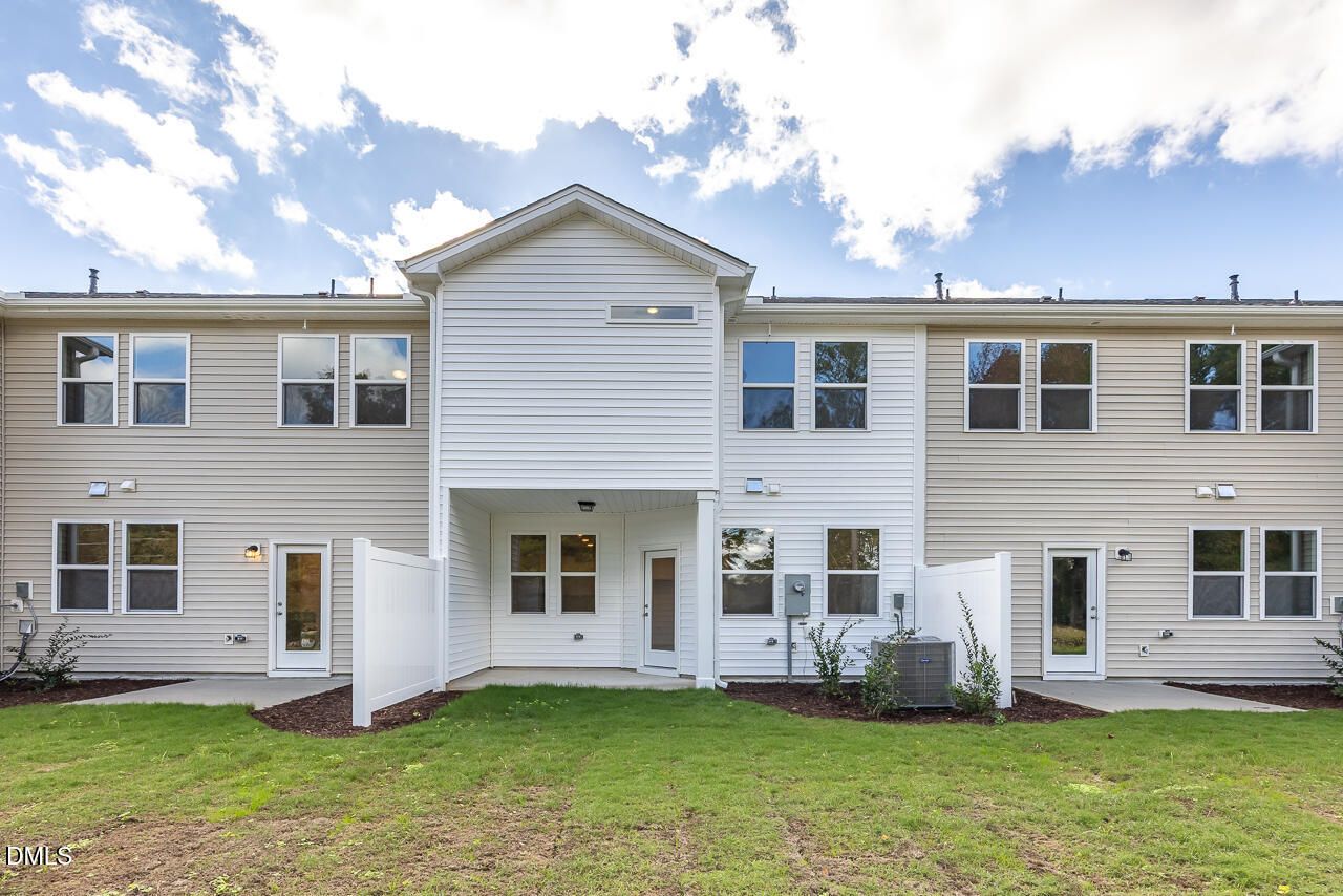 Rear view of two-story Graham Interior home with covered back patio, privacy fences, and green yard in Springvale, Fuquay-Varina, NC