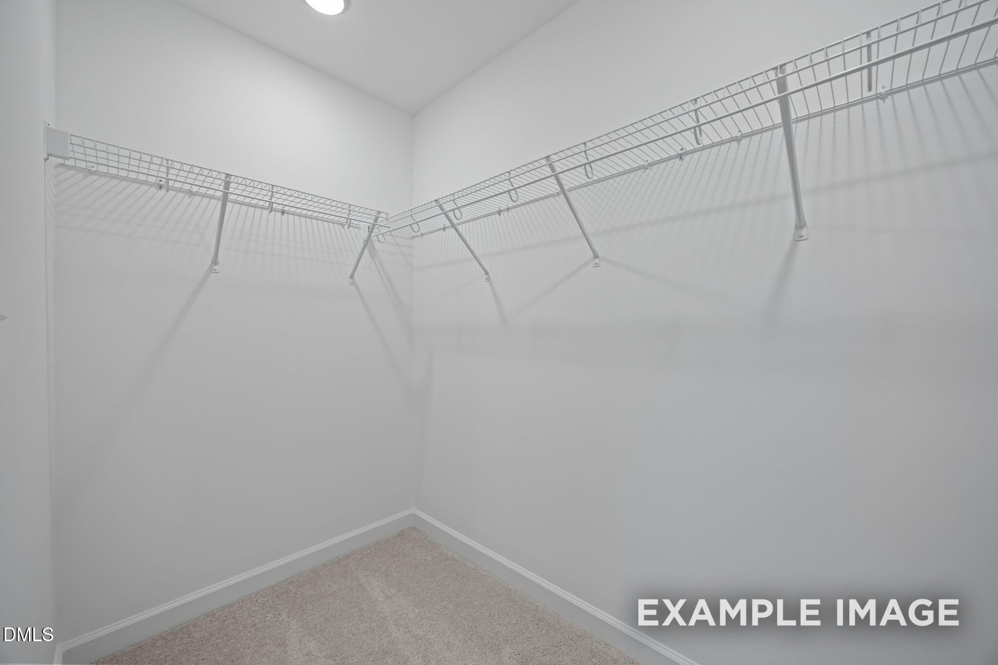 Spacious walk-in closet featuring wire shelving along white walls and carpeted floor in Davidson Homes The Avery, Knightdale, NC