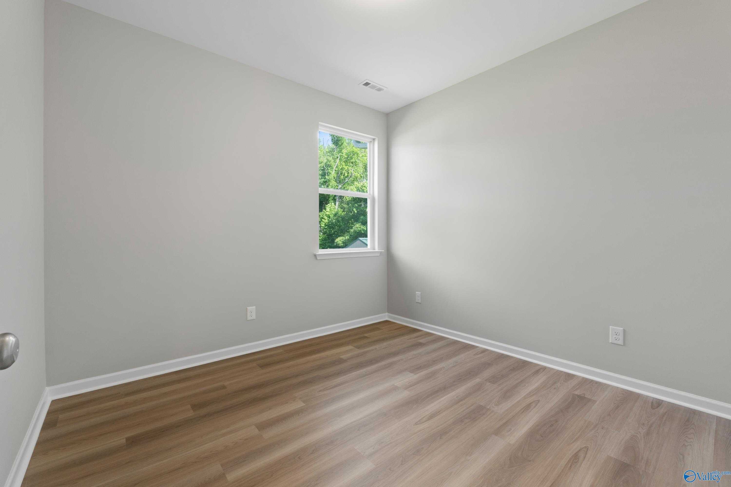 Bright secondary bedroom featuring light gray walls, large window with tree view, and hardwood floors in Davidson Homes The Polaris, Fayetteville, TN