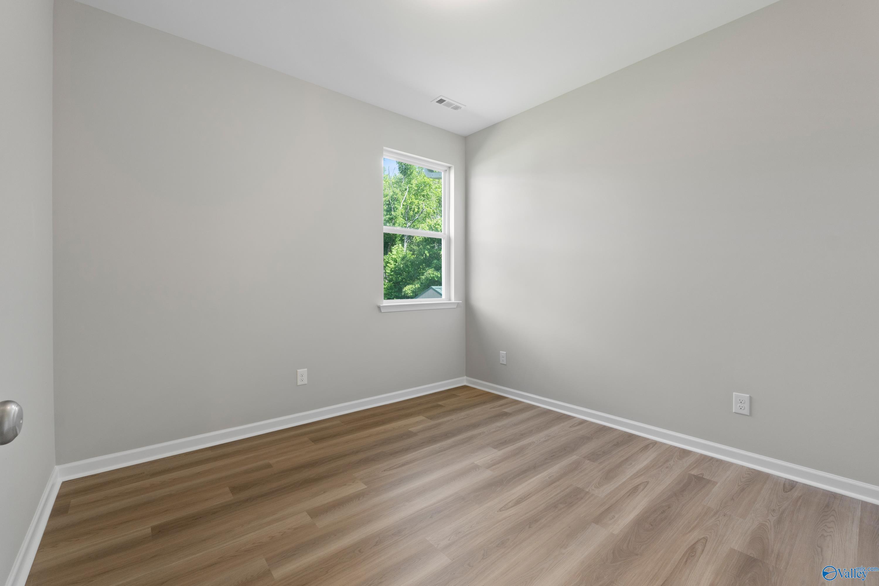 Bright secondary bedroom with light gray walls, large window overlooking trees, and luxury vinyl plank flooring in Davidson Homes The Polaris, Fayetteville, TN
