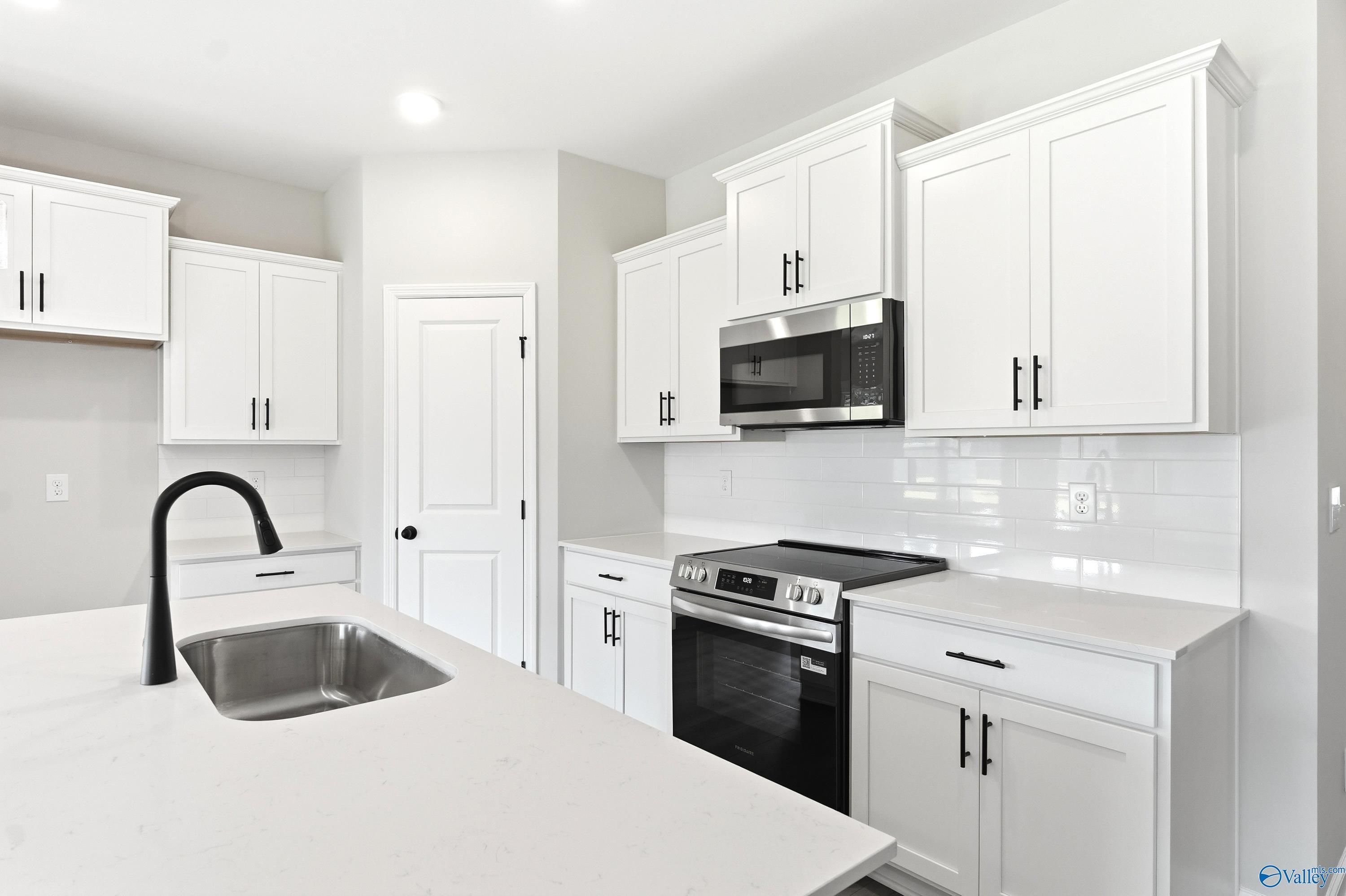 Modern kitchen with white cabinets, quartz countertops, and stainless appliances in The Daphne C, Flint Meadows home.