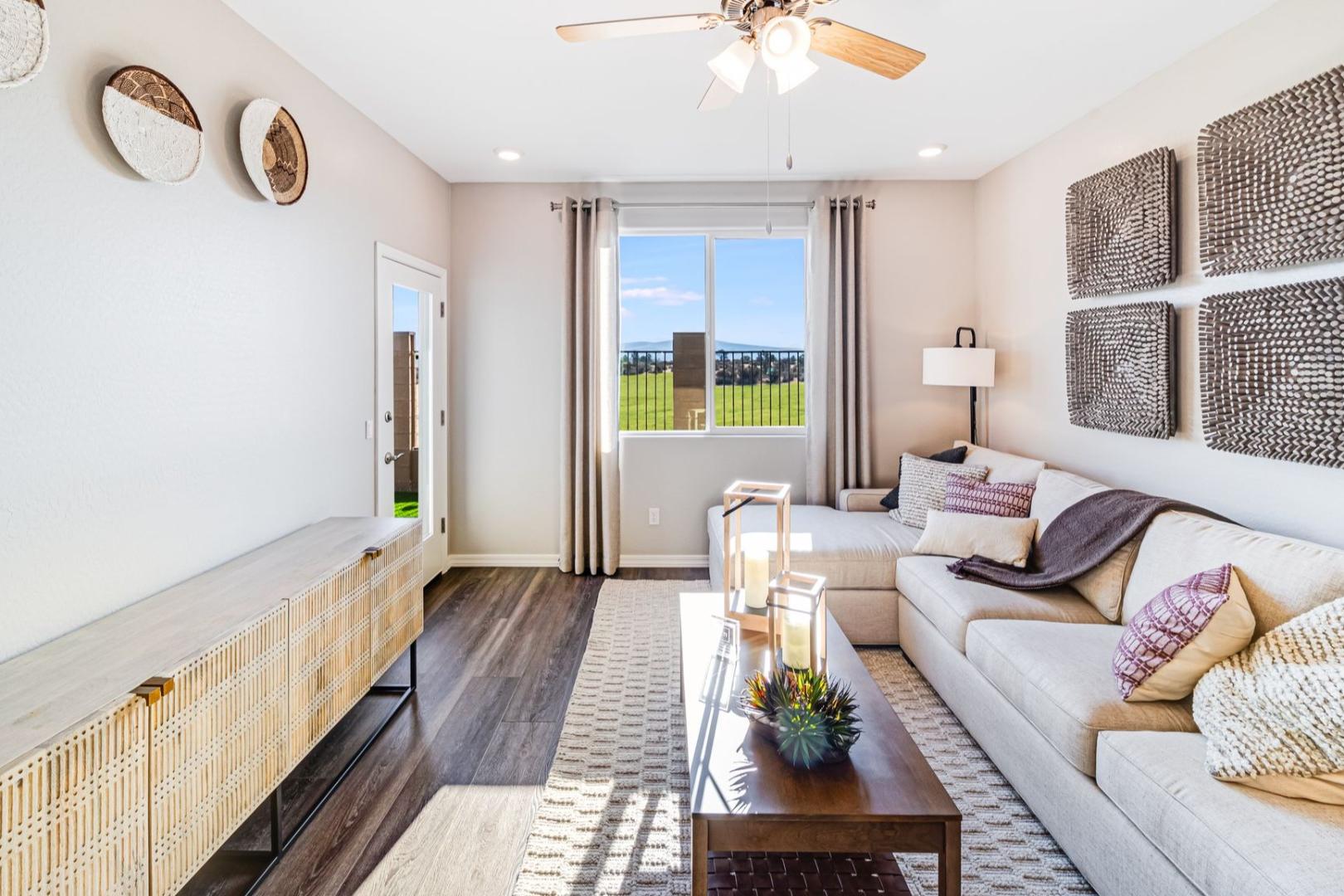 Cozy living room in The Savannah B showcasing L-shaped sofa, woven wall art, and Prescott Arizona mountain view