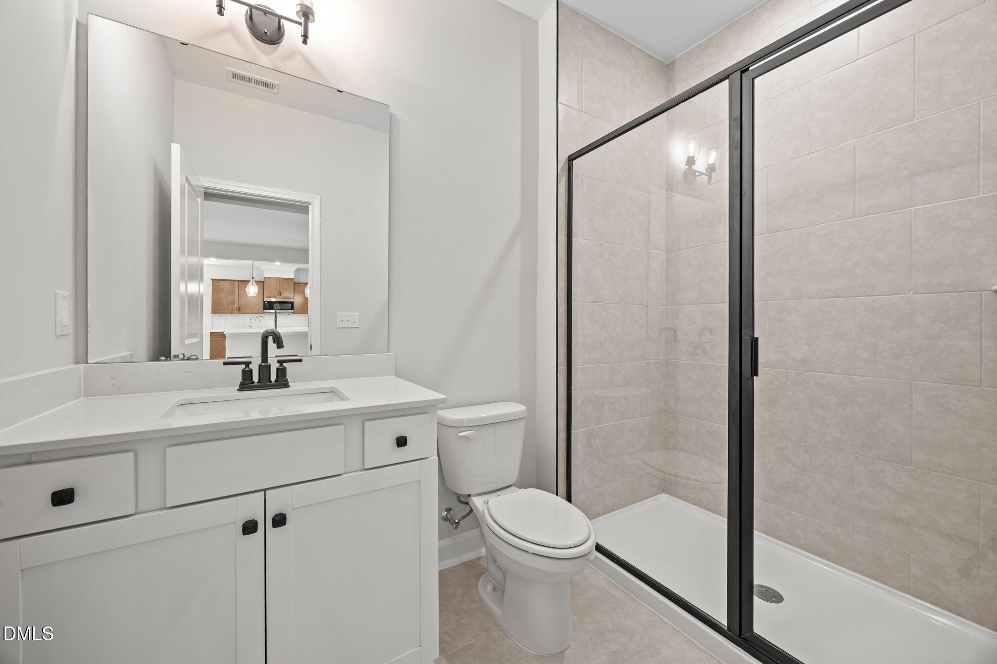 Modern white quartz vanity, black faucet, toilet, and glass-enclosed shower with beige tiles in The Willow D 4-bedroom home, Wendell, NC