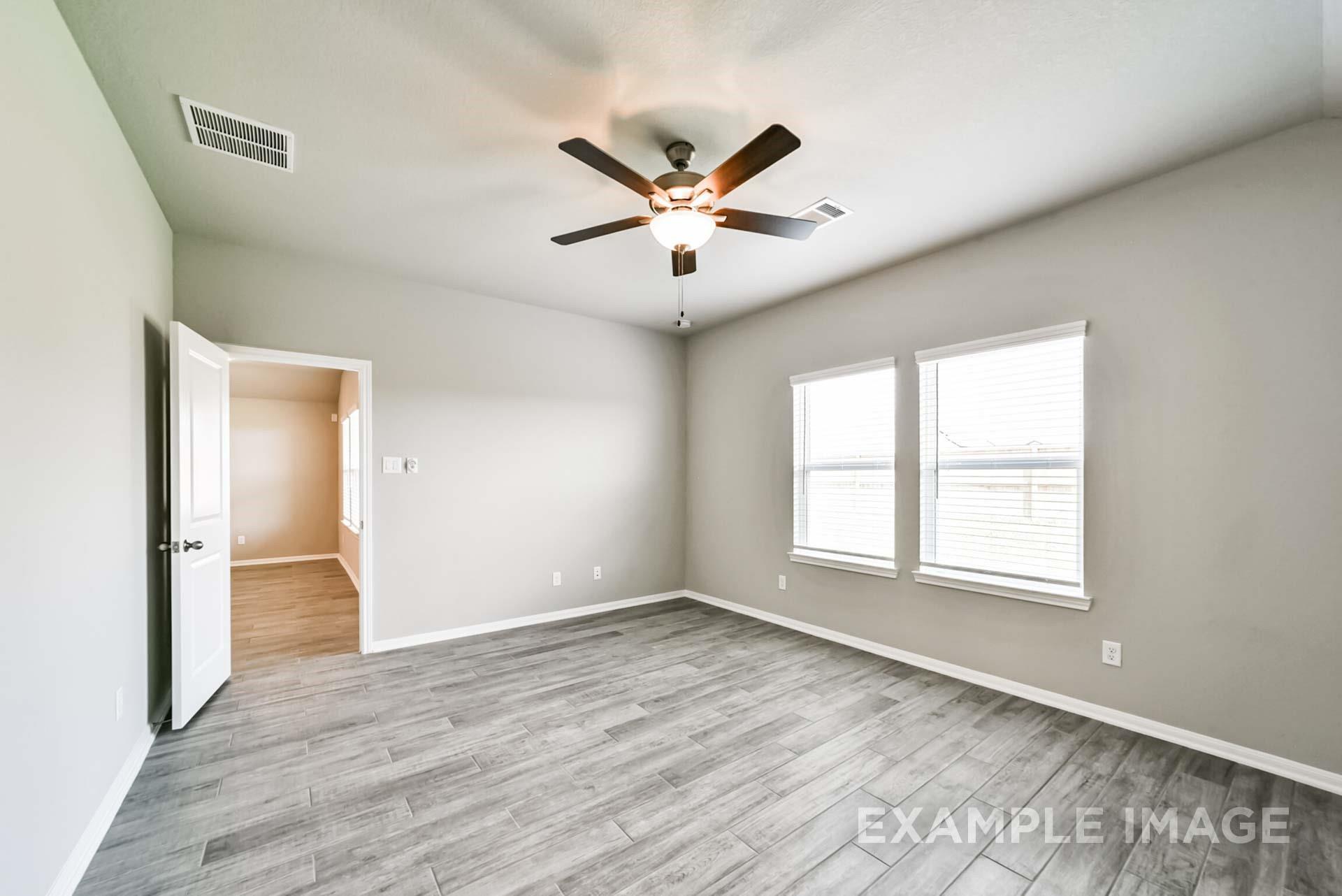 Spacious bedroom with gray wood-look tile flooring and ceiling fan in The Riviera A floor plan at Emberly, Beasley, TX.