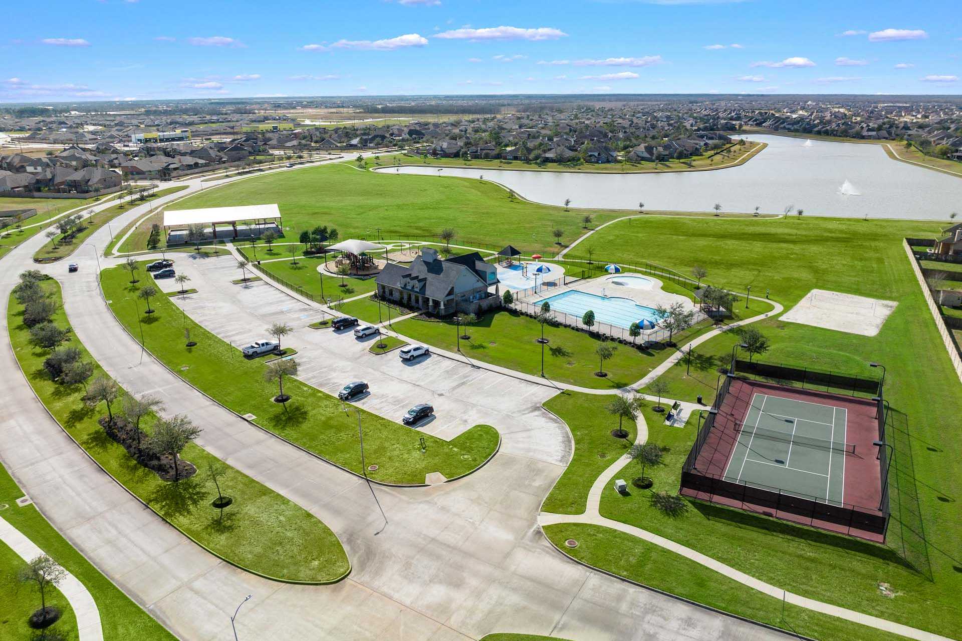 Aerial view of Sierra Vista clubhouse, resort pool, and tennis court in Rosharon TX by Davidson Homes with green lawns and lake