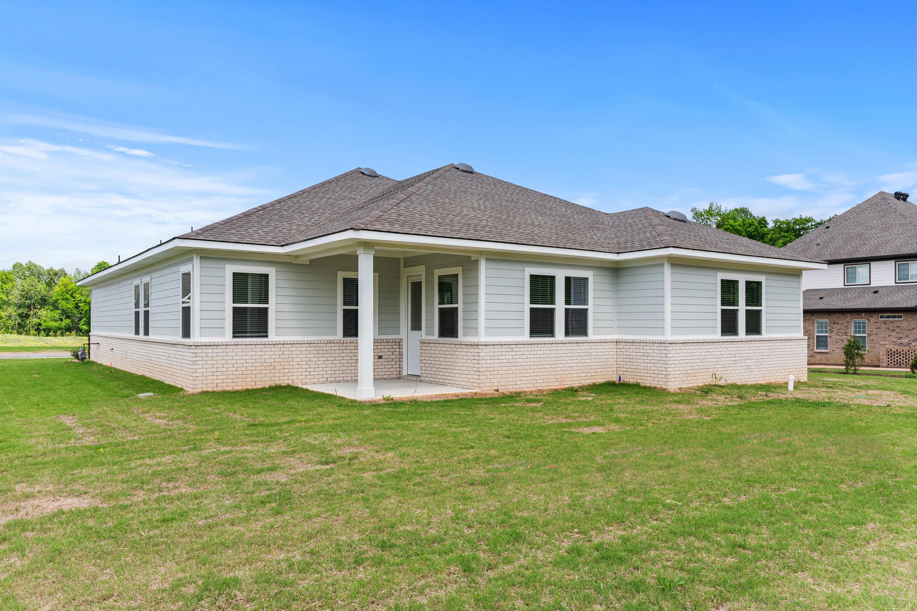 Single-story exterior of The Arcadia B showcasing beige siding, dark shingle roof, covered porch, and lush green yard