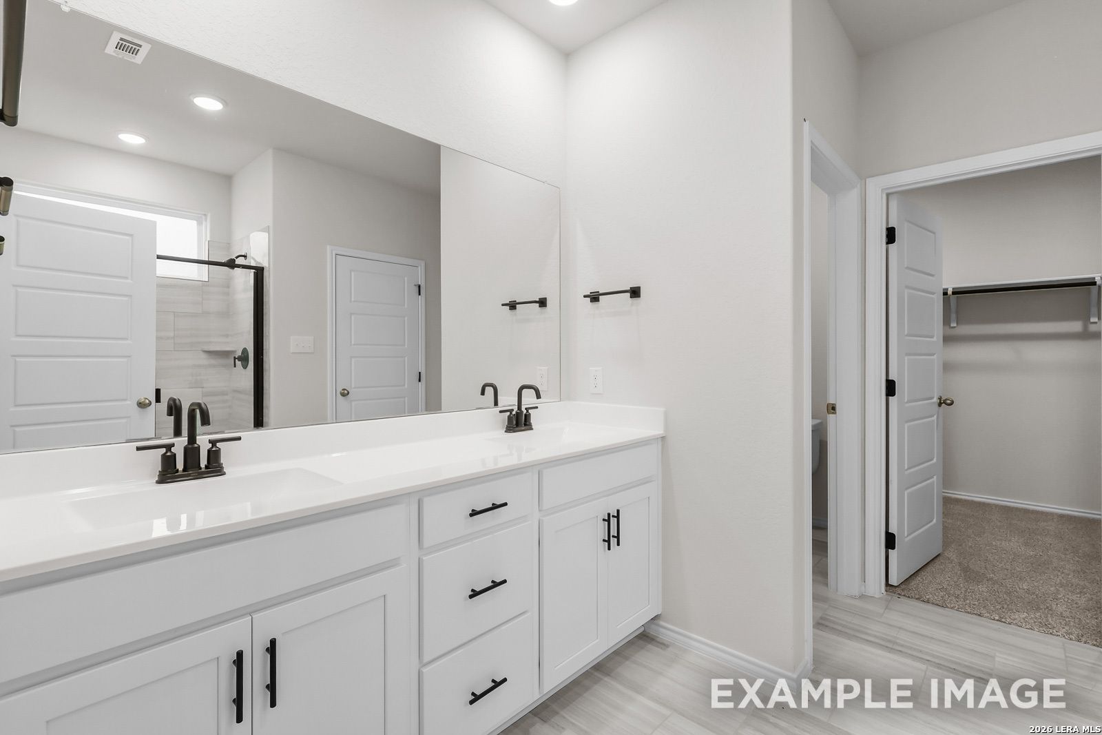 Modern bathroom with double vanity, sleek black fixtures, and walk-in closet in The Sequoia C at Royal Crest, San Antonio.