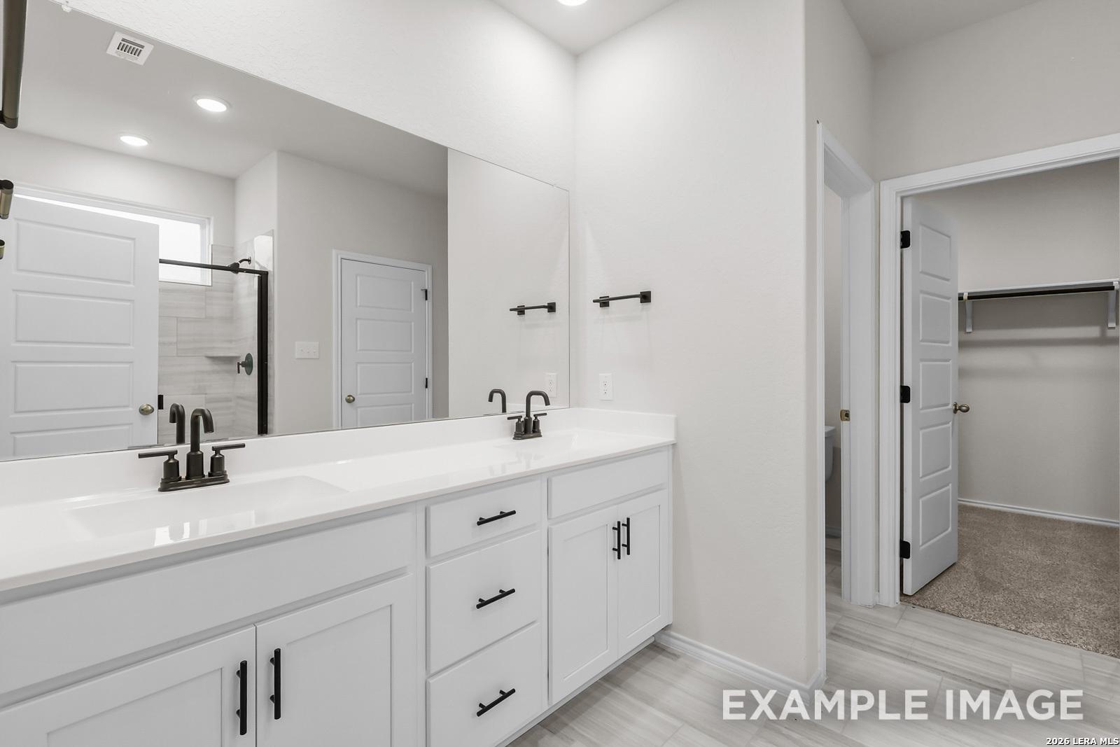 Modern bathroom with double vanity, sleek black fixtures, and walk-in closet in The Sequoia C at Royal Crest, San Antonio.