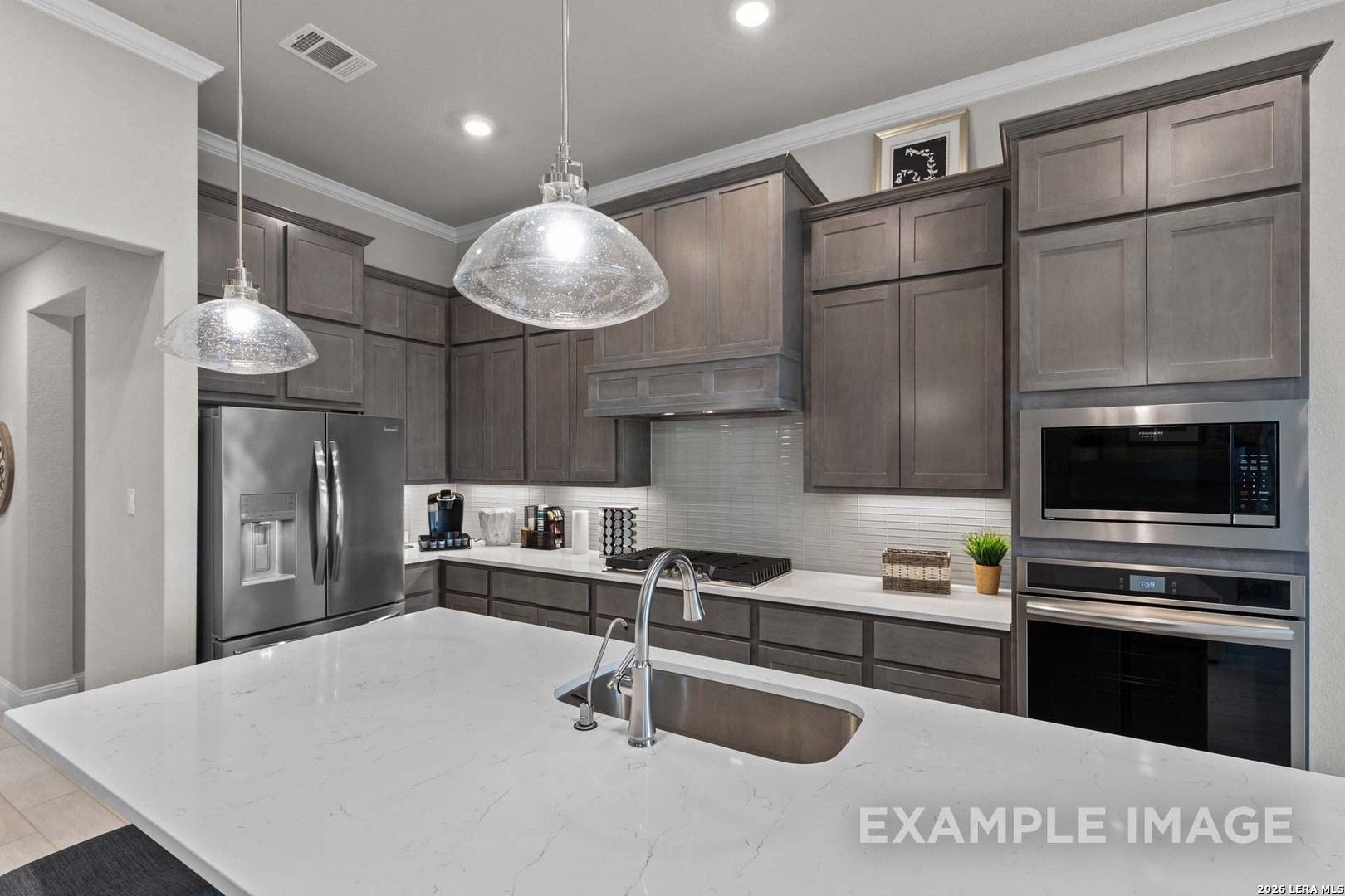 Modern kitchen with gray cabinets, quartz countertops, and stainless appliances in The Garner C plan, Castroville, Texas.