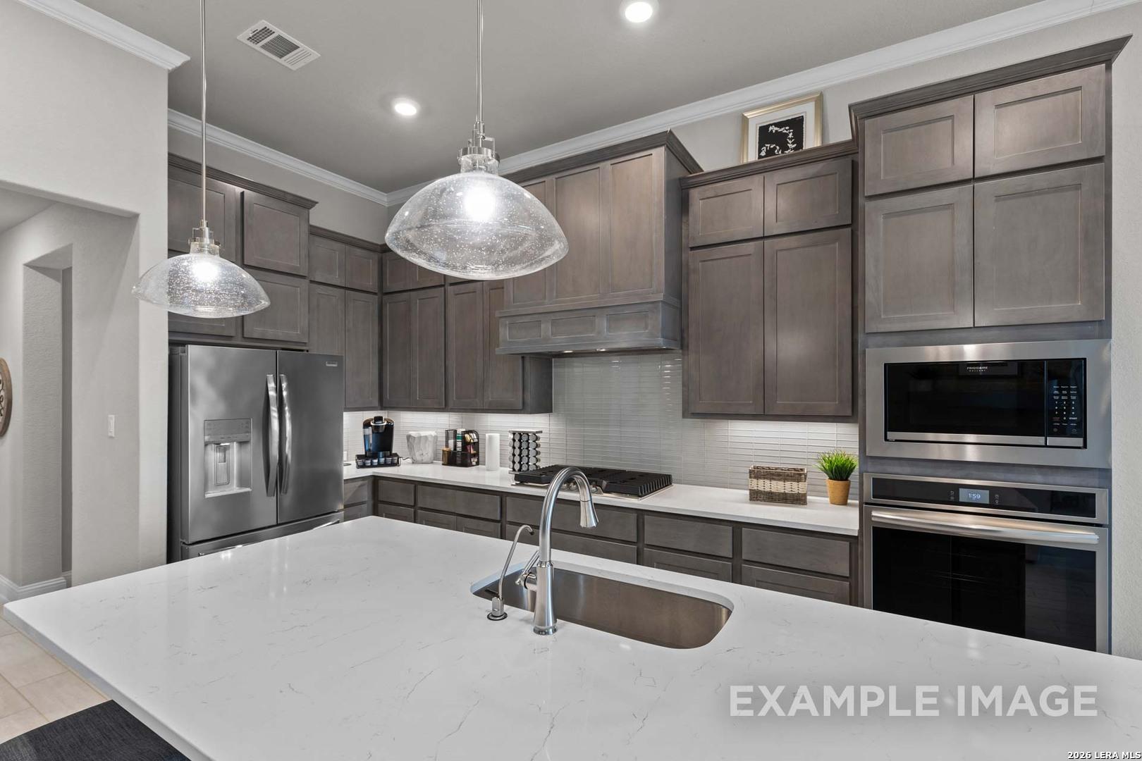 Modern kitchen with gray cabinets, quartz countertops, and stainless appliances in The Garner C plan, Castroville, Texas.