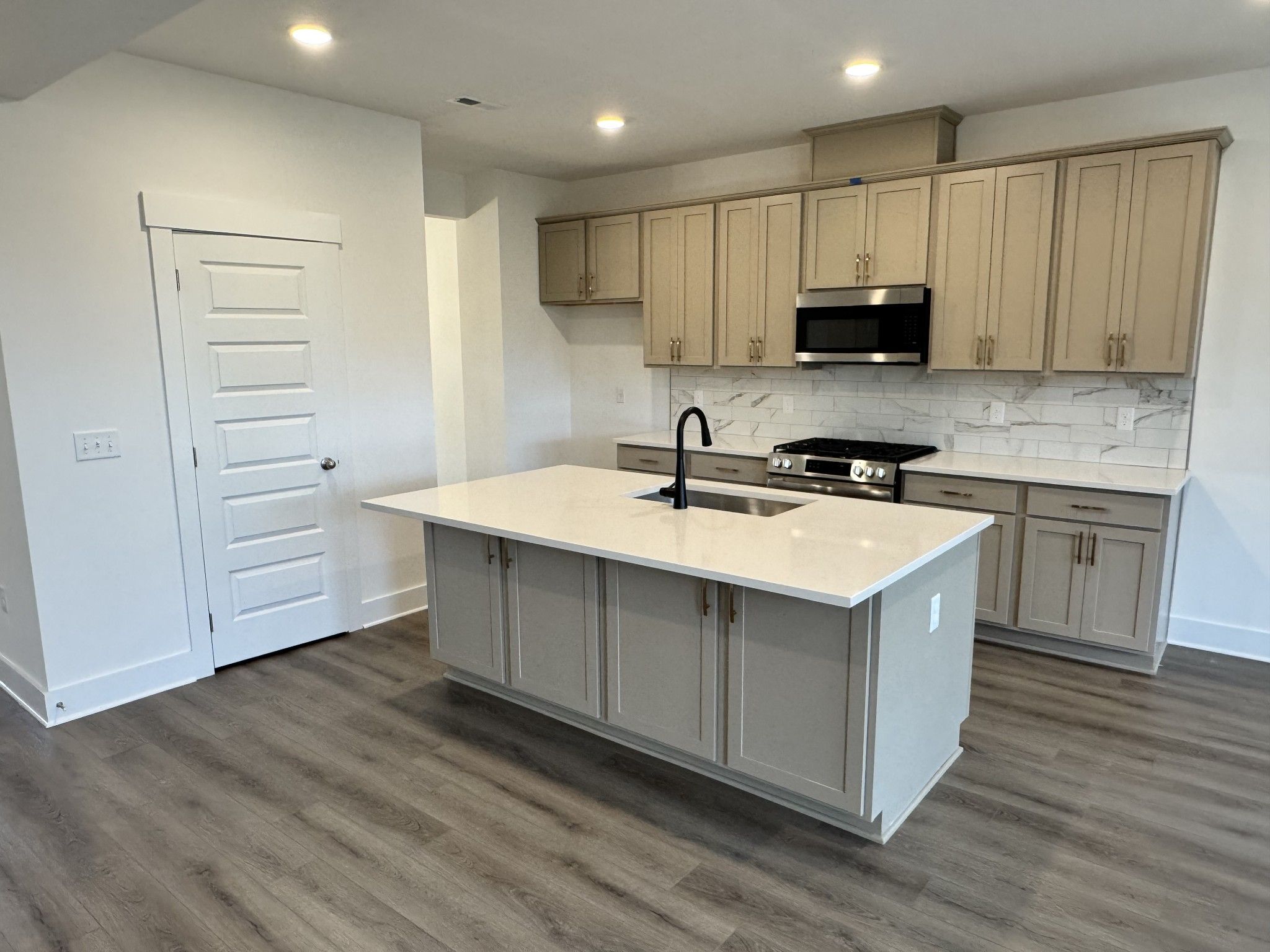 Kitchen island with sink, beige cabinetry, marble tile backsplash, and stainless gas range in Davidson Homes The Willow B, Gallatin, TN