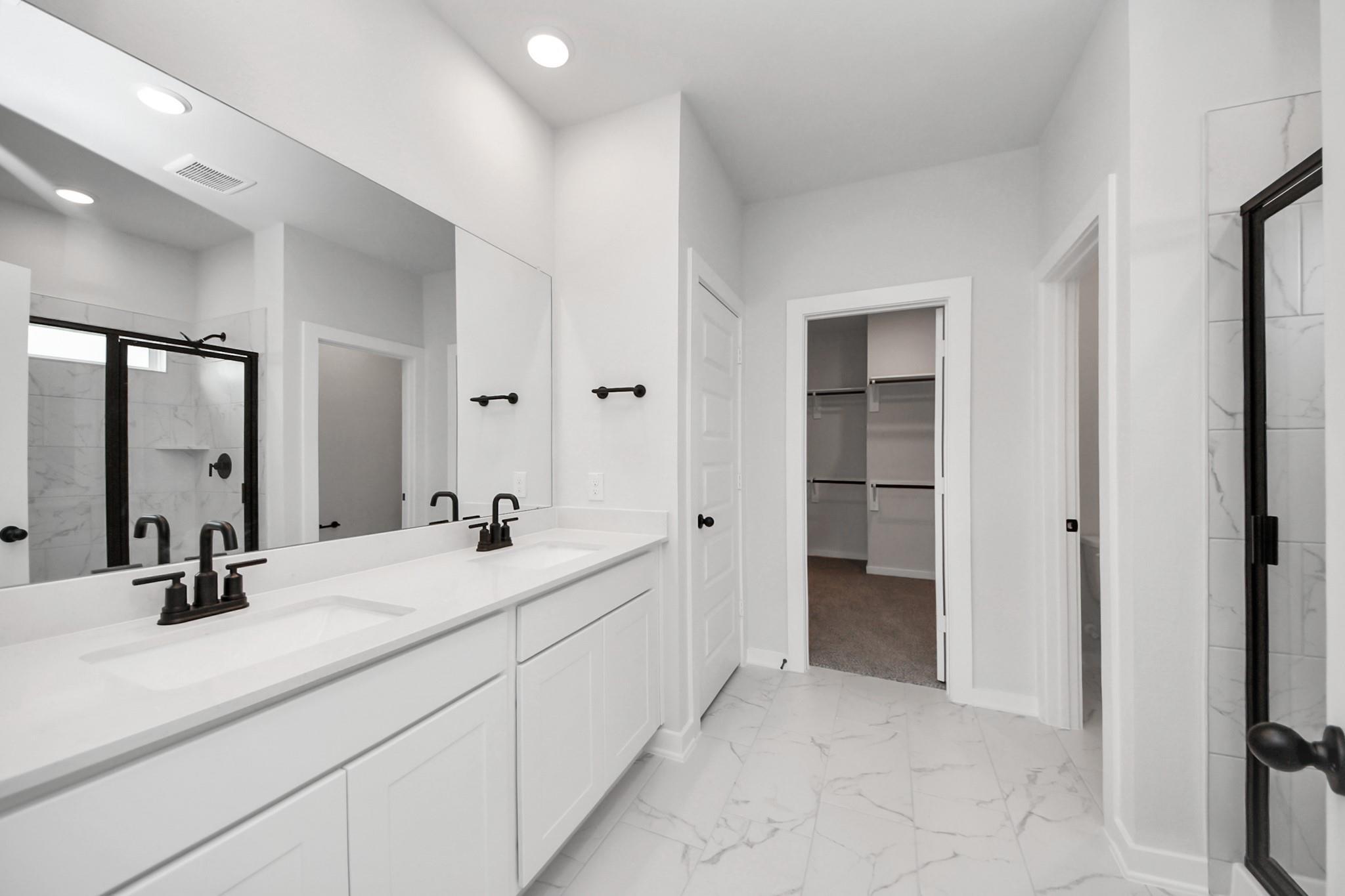 Modern primary bathroom with double vanity, walk-in closet, and glass-enclosed shower in The Everett C, River Ranch Meadows.