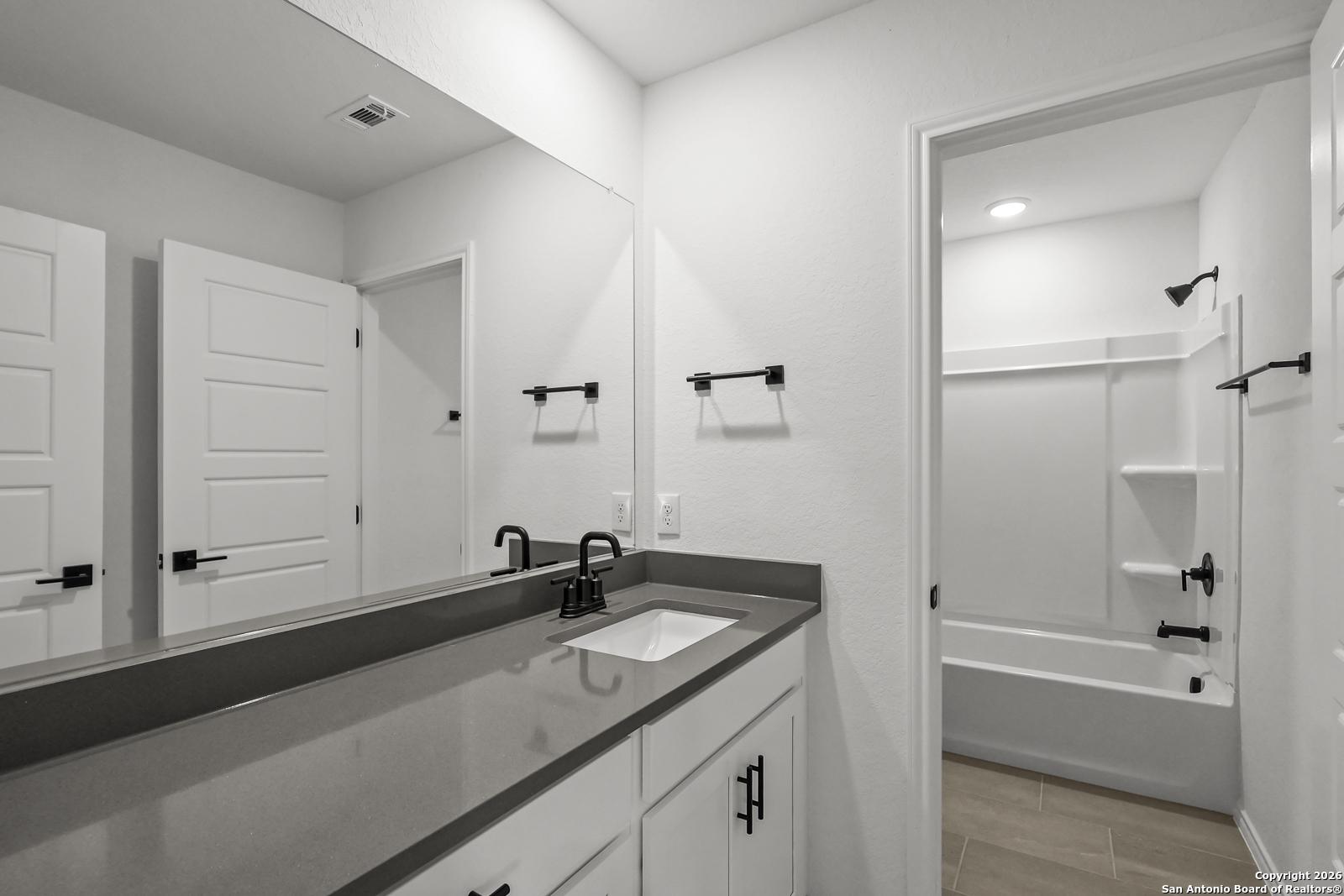 Modern double vanity bathroom with gray quartz countertop, white cabinets, and soaking tub in Davidson Homes The Douglas E, San Antonio