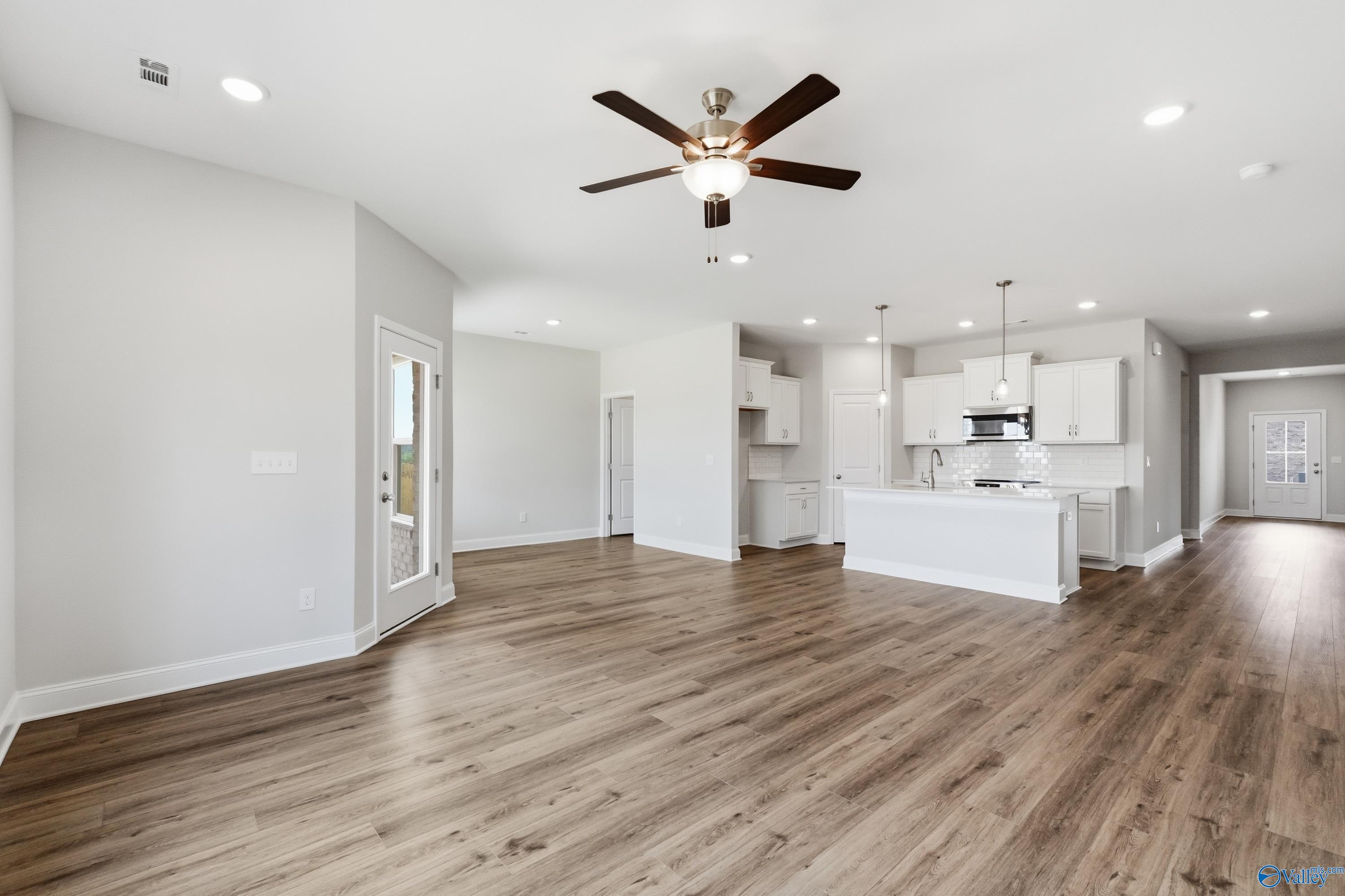Open-concept living and kitchen area with hardwood floors, white cabinets, and ceiling fans in Davidson Homes The Daphne C, Toney, Alabama