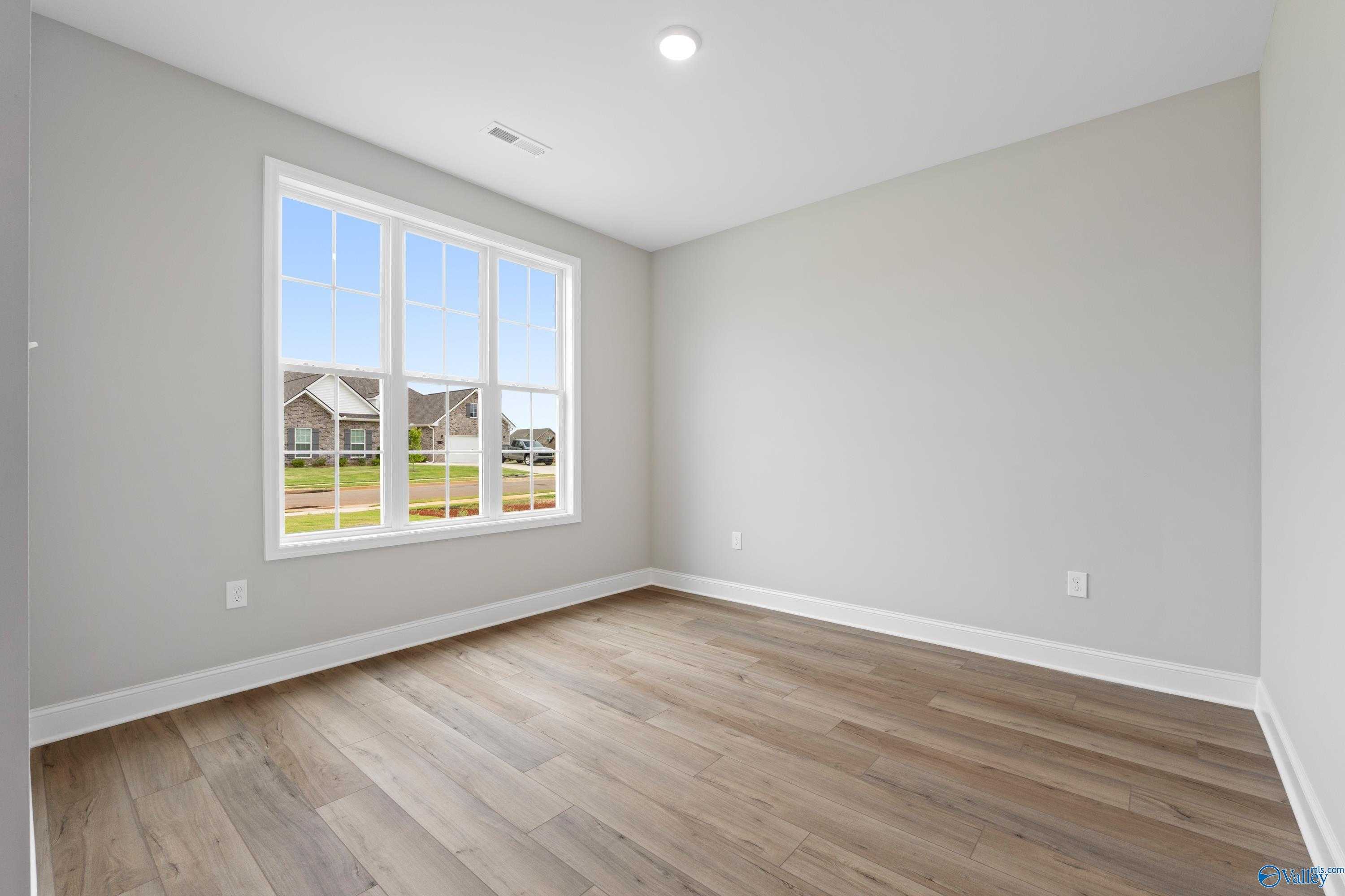 Bright empty bedroom with large window overlooking green lawn and homes, light wood floors, neutral walls in The Finleigh, Meridianville, AL