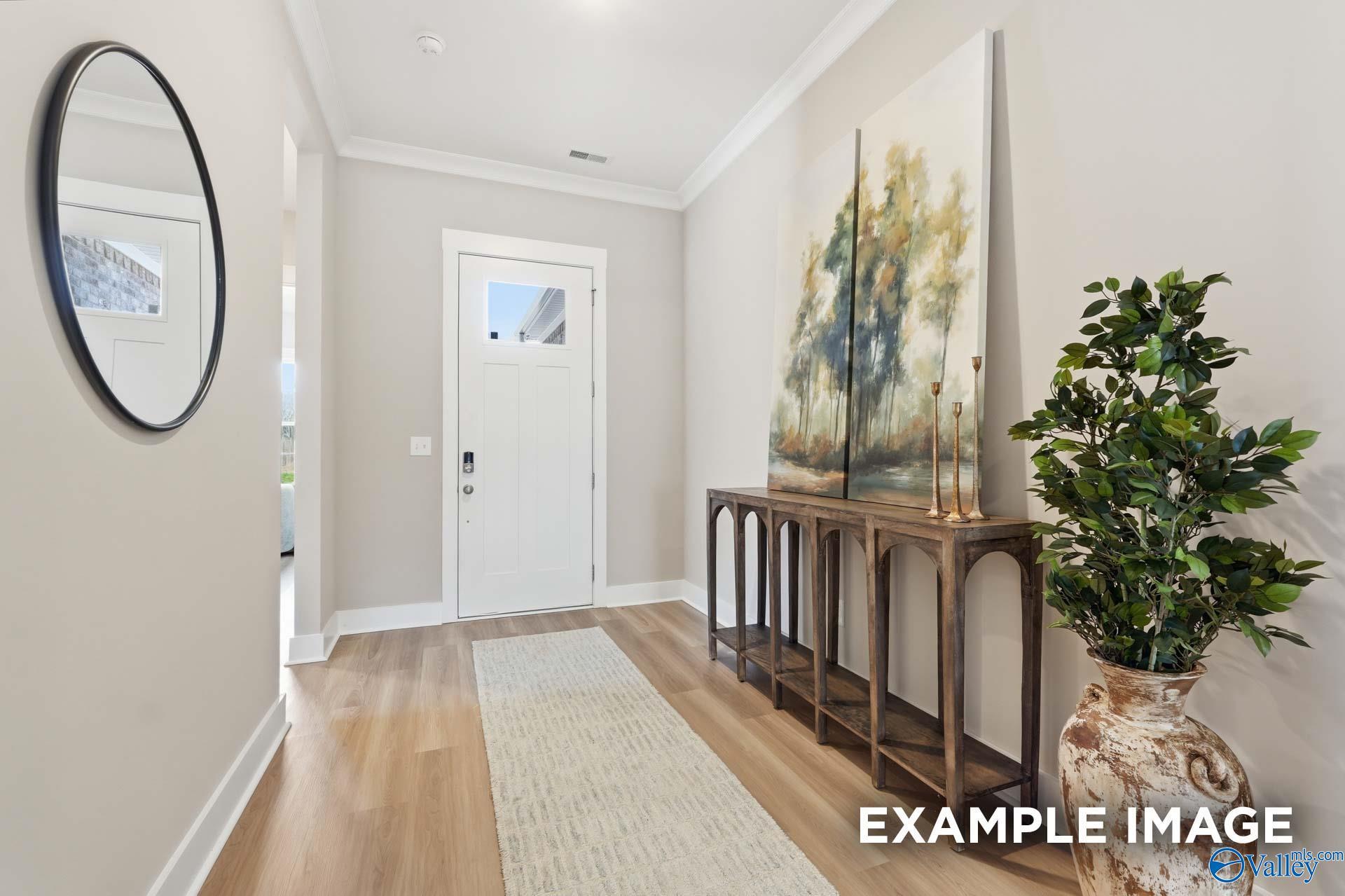 Elegant entry hallway with round mirror, white paneled door, console table, abstract tree painting, and potted plant in Evermore Homes The Oxford B, Owens Cross Roads, Alabama