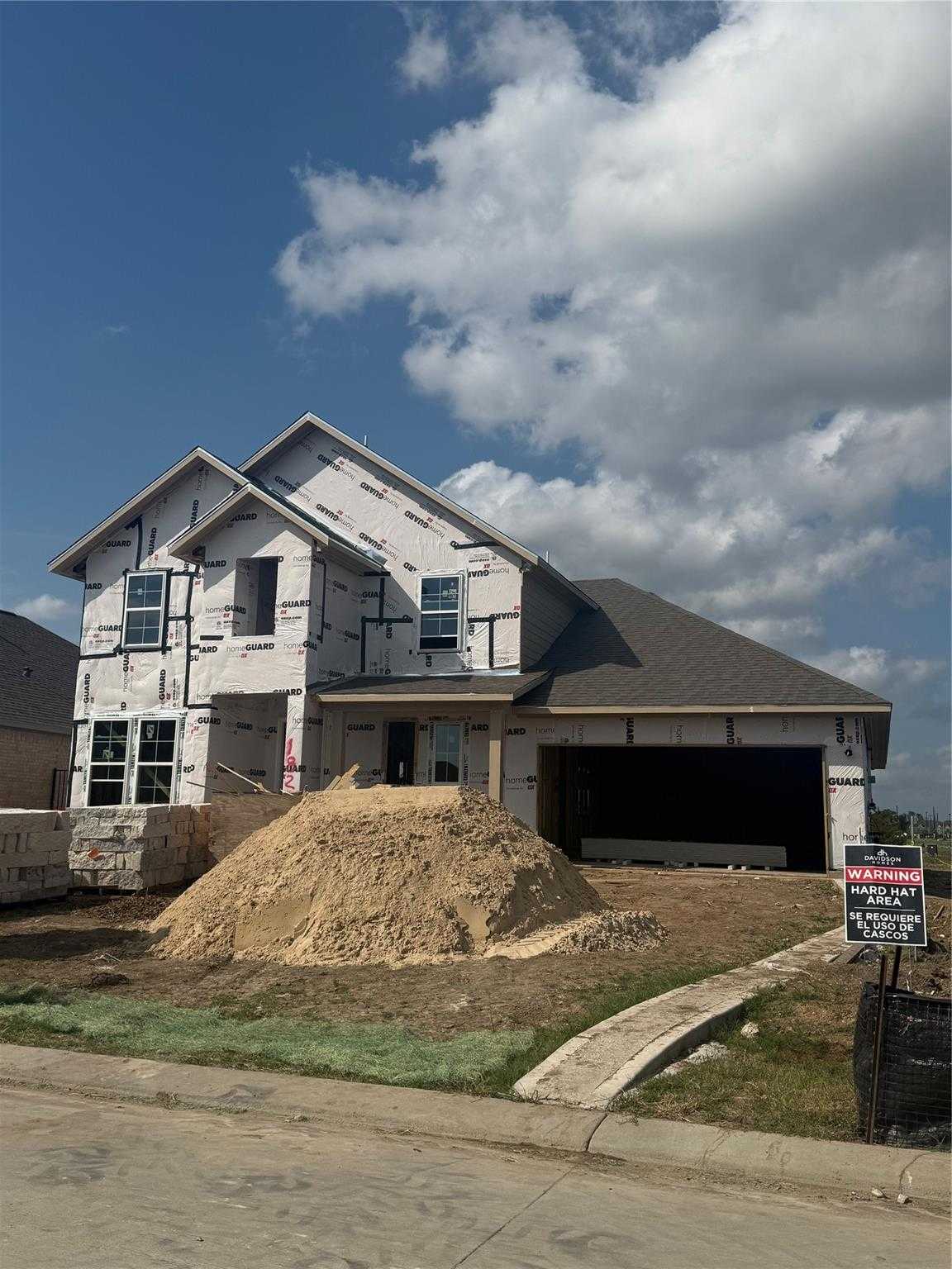New construction framed 4-bedroom home with 3-car garage, for sale sign, and sand pile in Sierra Vista, Rosharon, Texas - Davidson Homes Philip C