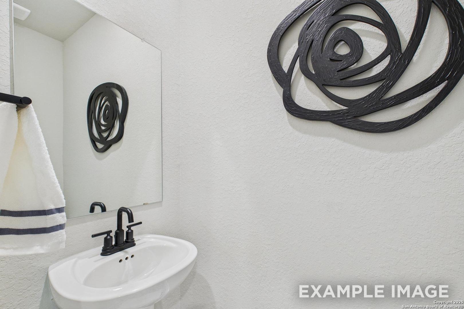 Modern powder room featuring white pedestal sink, black rose wall art, and towel on sleek holder in Davidson Homes The Charlotte B, San Antonio