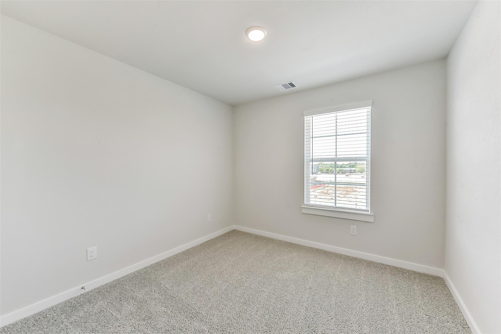Bright empty bedroom with light gray carpet, white walls, and window blinds in Davidson Homes The Brazos E, Magnolia, Texas