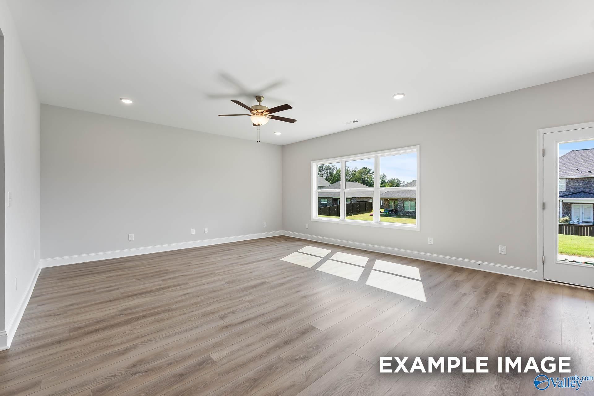 Bright living room with large windows, ceiling fan, and French doors to backyard in The Chelsea D home, New Market, Alabama