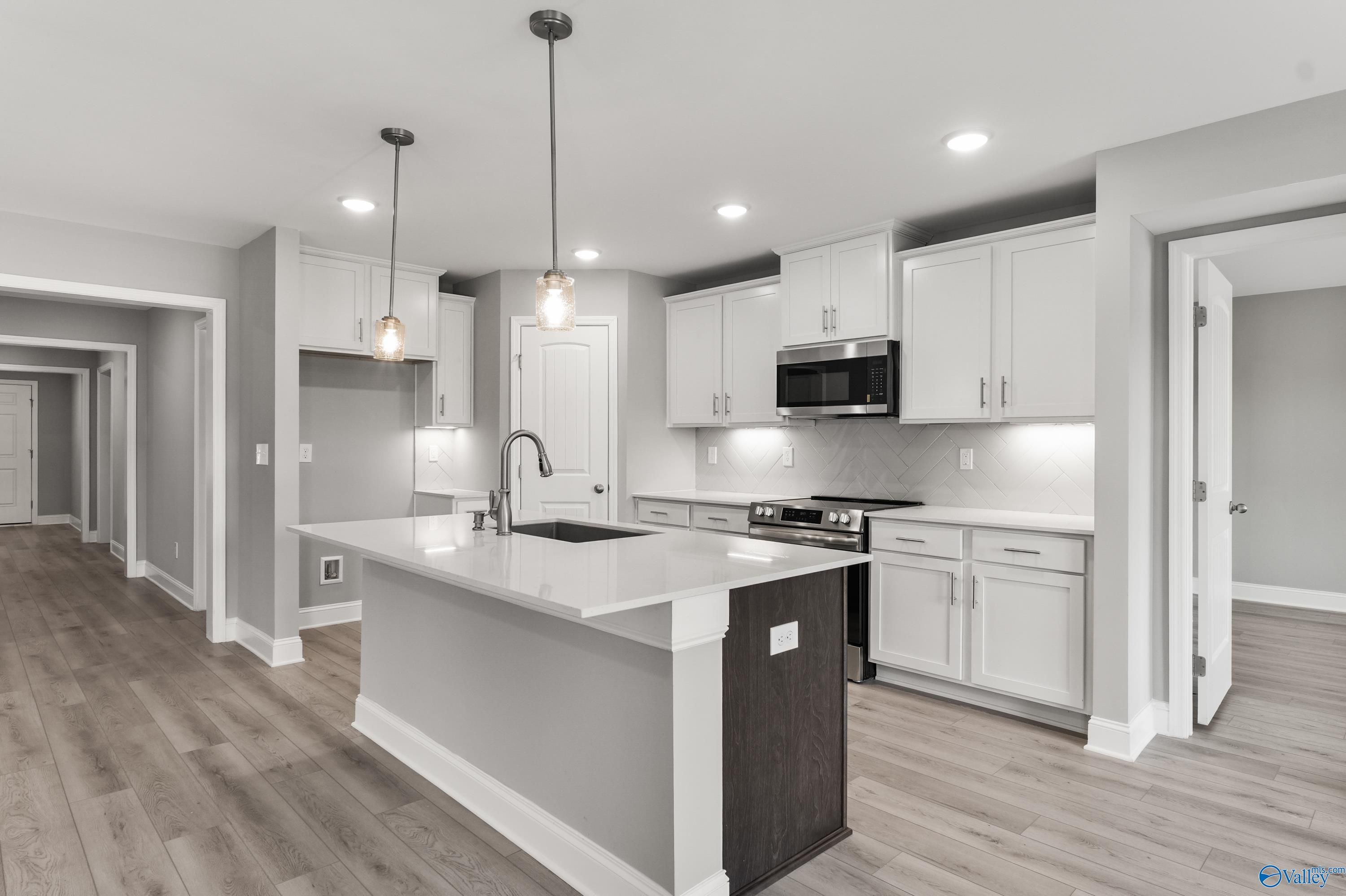 Modern white kitchen with quartz island, stainless appliances, pendant lights in The Everett B floor plan, Athens, Alabama