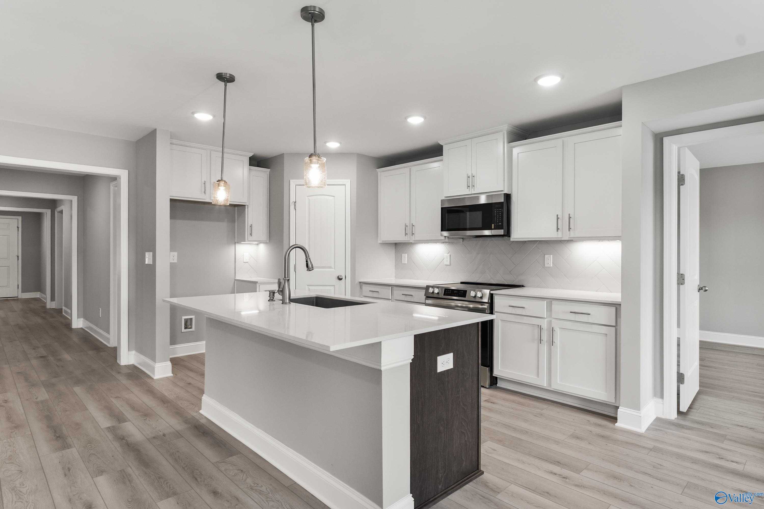 Modern white kitchen with quartz island, stainless appliances, pendant lights in The Everett B floor plan, Athens, Alabama