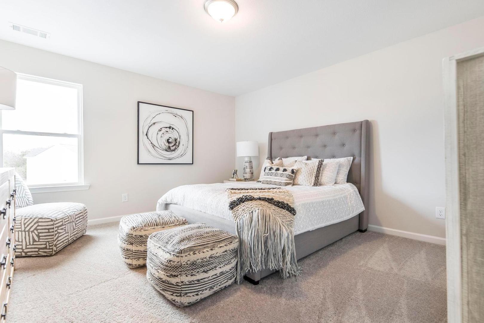 Spacious bedroom at Cape Reserve in Donahue Ridge, Auburn AL with gray tufted bed, neutral decor, and abstract wall art