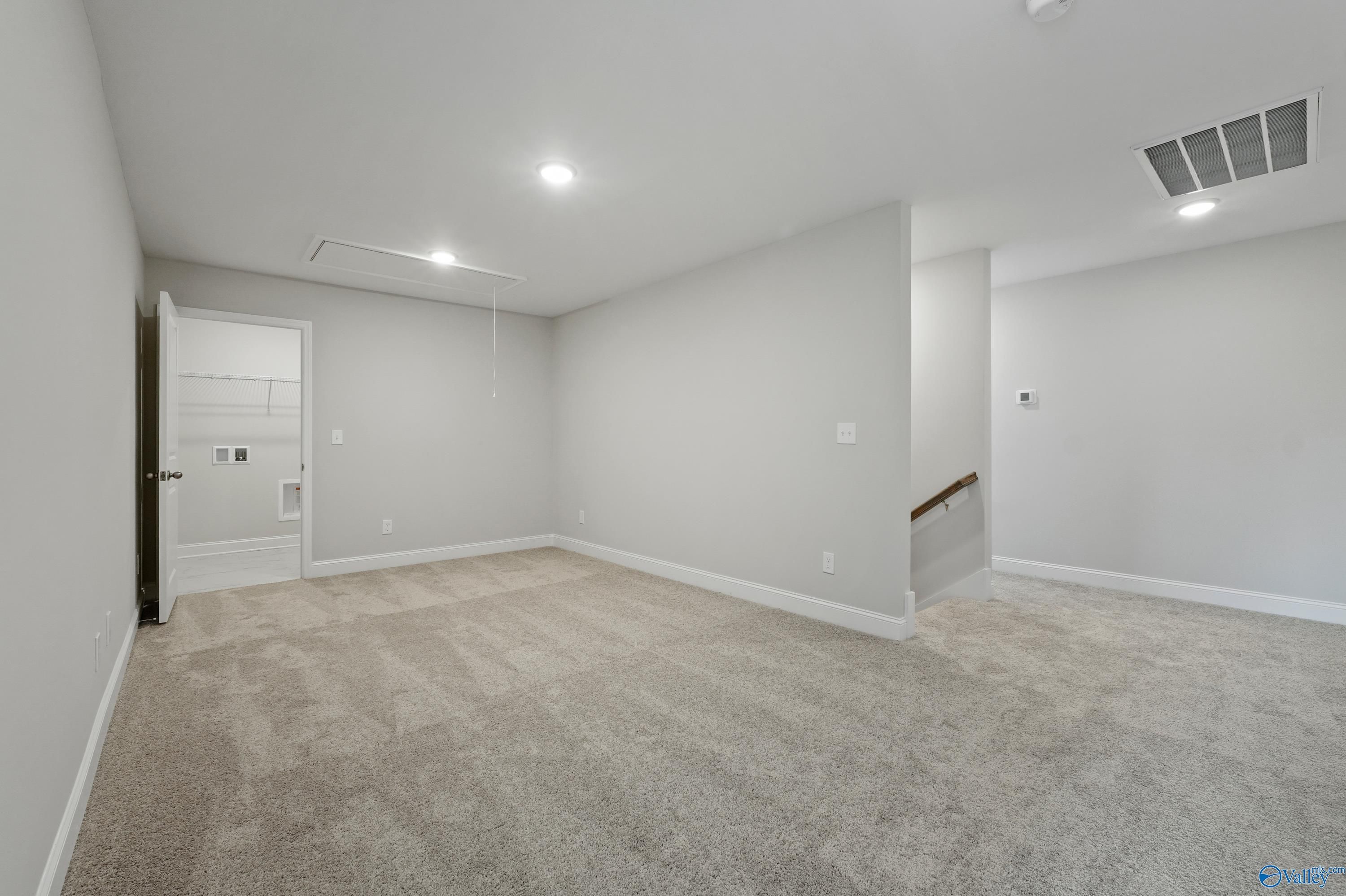 Spacious upstairs bonus room with light gray walls, beige carpet, staircase, and open doorway in The Camden B by Davidson Homes, Huntsville