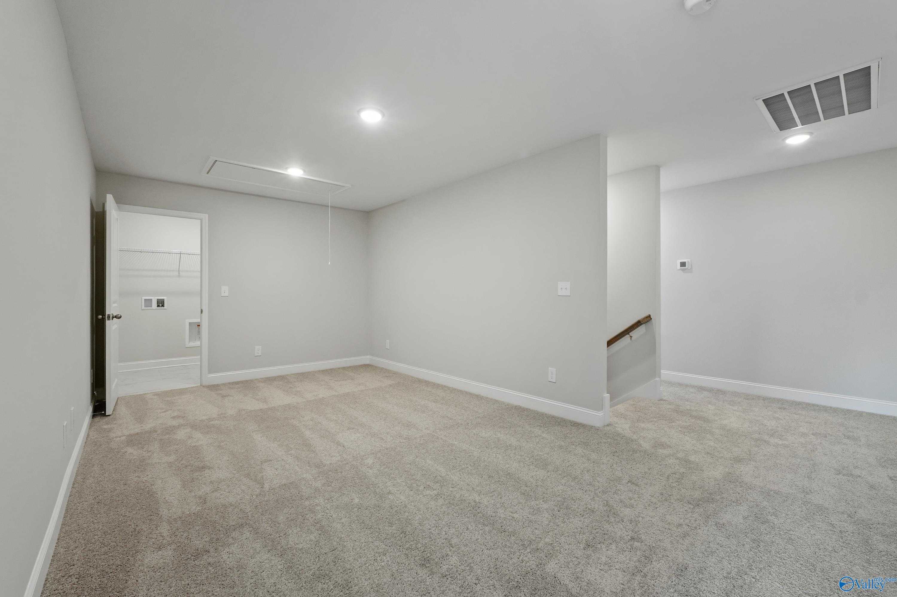 Spacious upstairs bonus room with light gray walls, beige carpet, staircase, and open doorway in The Camden B by Davidson Homes, Huntsville