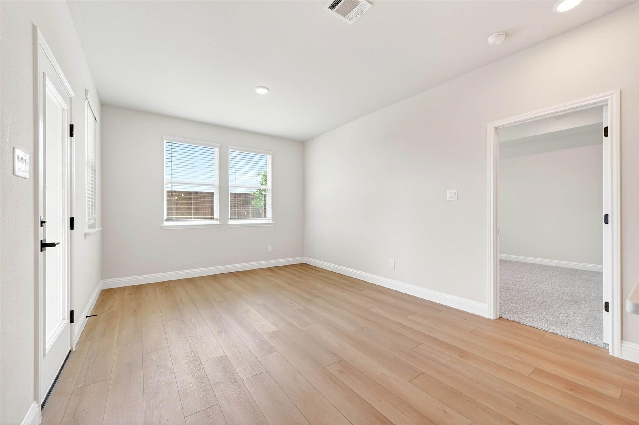 Bright, neutral living space with wood-style flooring and backyard access in The Holly C floor plan, Anna, Texas.