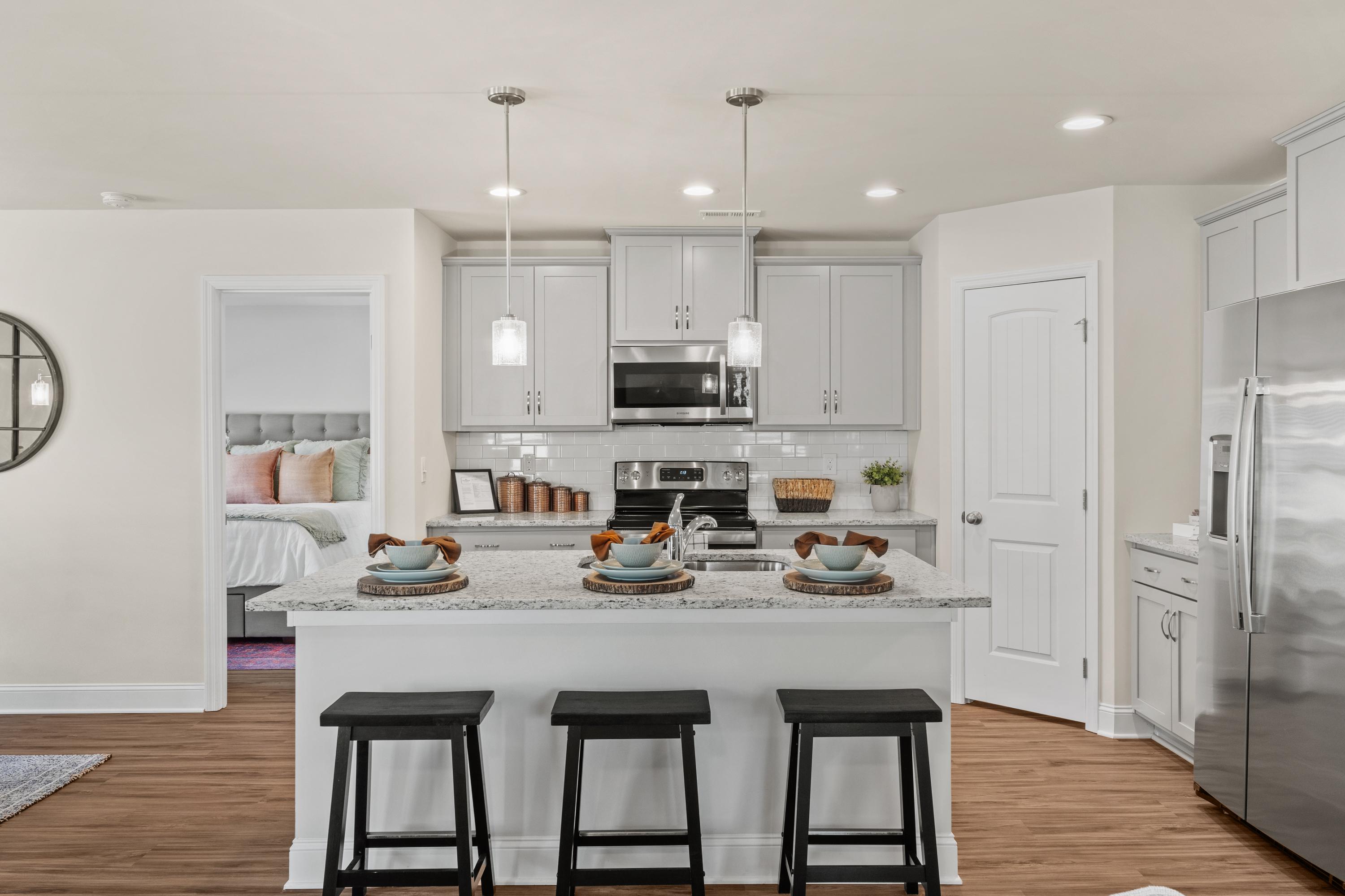 Spacious white kitchen at Berry Cove in New Market Alabama with island seating, stainless appliances, hardwood floors