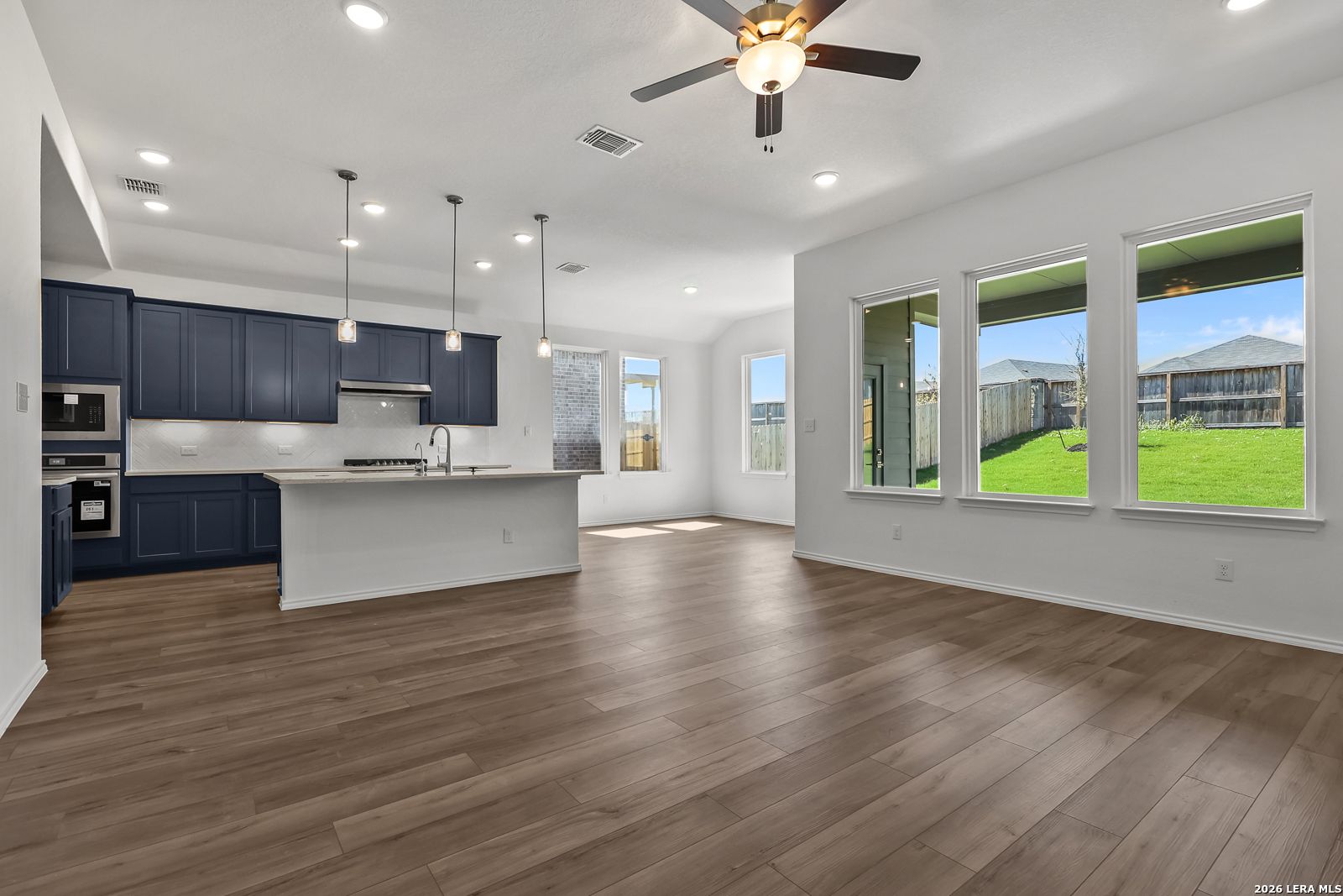 Modern navy kitchen with white island, stainless appliances, and open living area overlooking lush backyard in Davidson Homes The Sequoia B, San Antonio