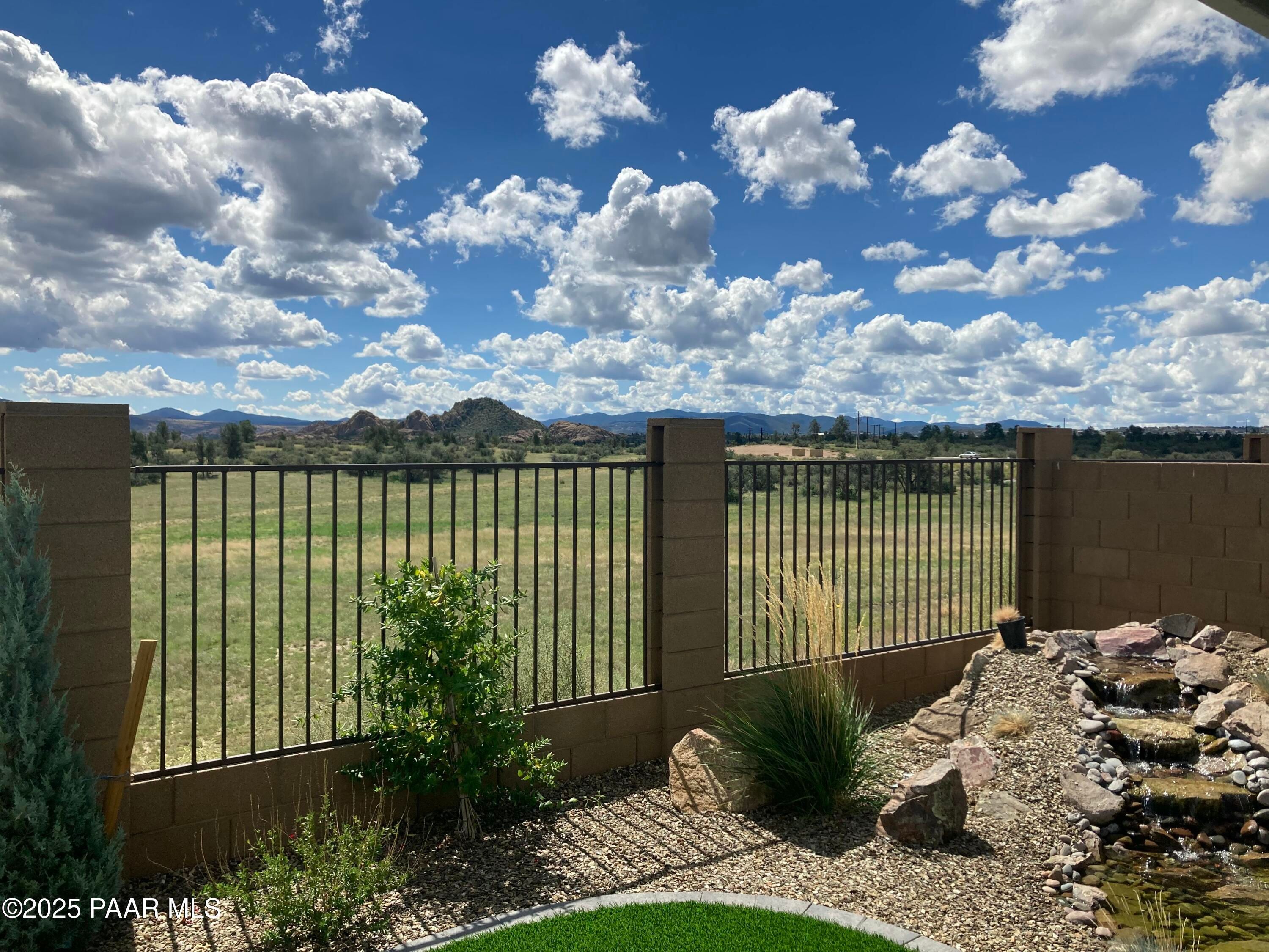 Scenic backyard with rock waterfall, desert plants, wrought iron fence, and mountain views in Prescott, Arizona home