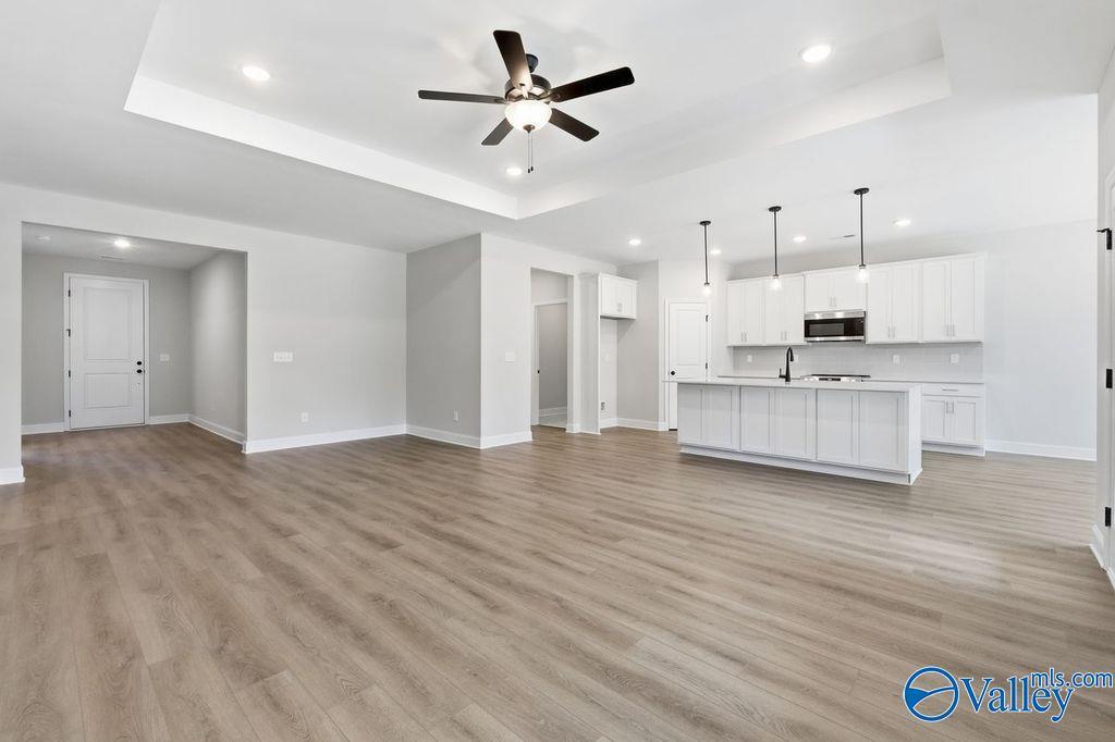 Spacious open-concept kitchen-living area with white cabinets, large island, stainless appliances, ceiling fan, hardwood floors in 3BR Montgomery B home, Hartselle, AL