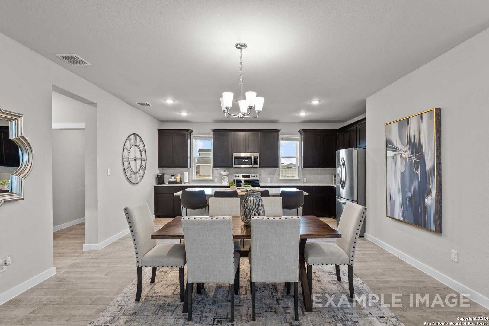 Modern dining area with open kitchen, dark cabinets, chandelier, and large windows in Davidson Homes The Collin A, Seguin, Texas