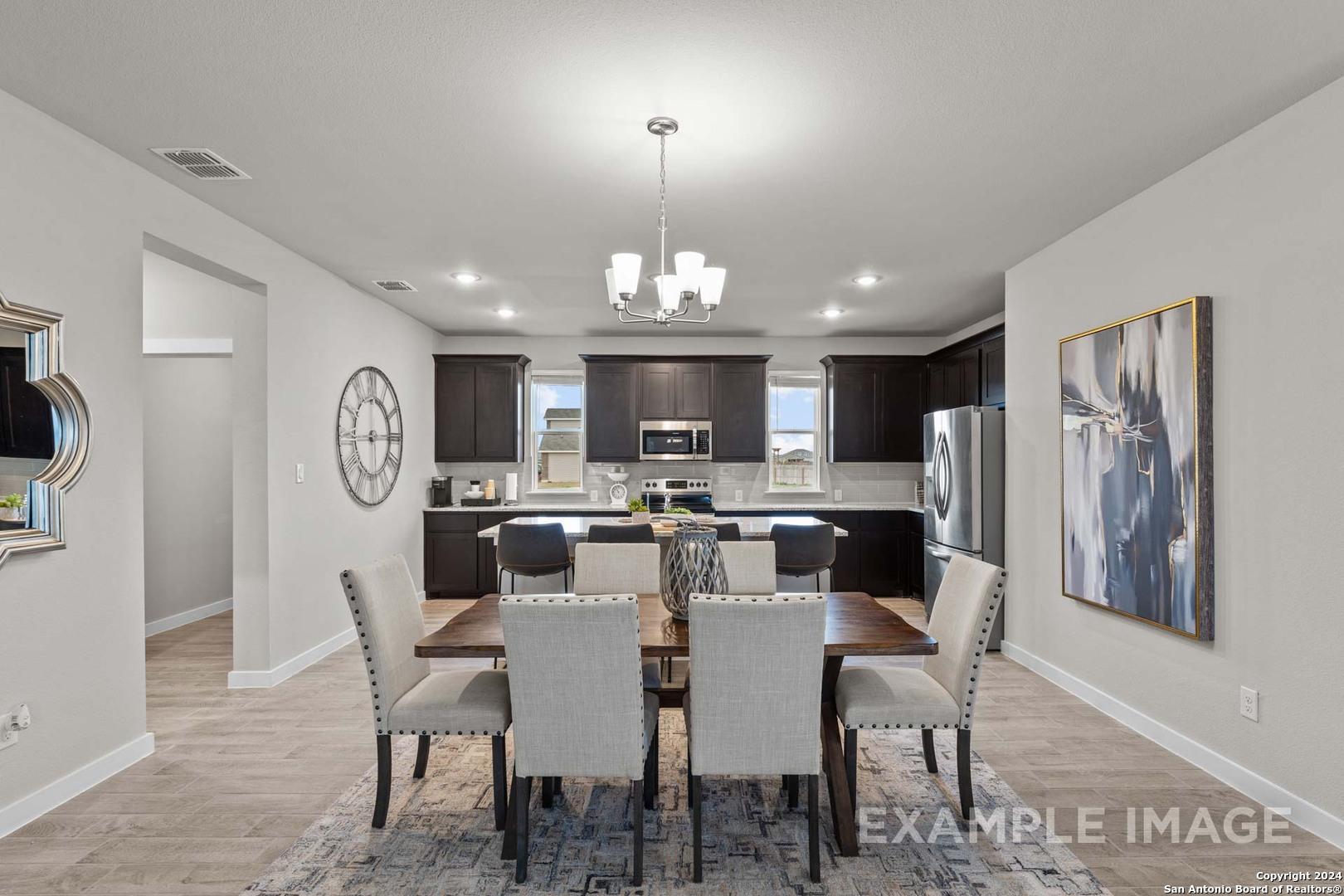 Modern dining area with open kitchen, dark cabinets, chandelier, and large windows in Davidson Homes The Collin A, Seguin, Texas