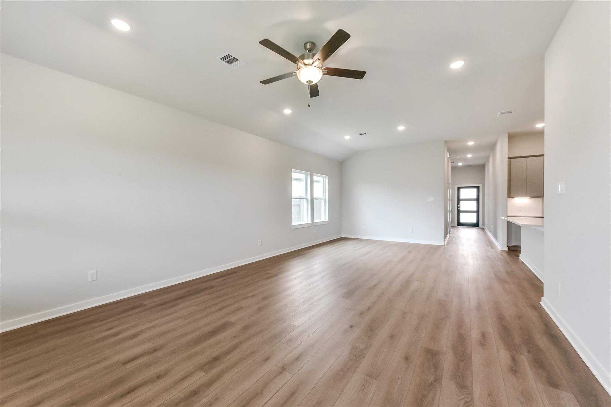 Expansive open living room with light wood floors, ceiling fan, recessed lights, and large windows in Davidson Homes The Laguna C, Rosharon, Texas