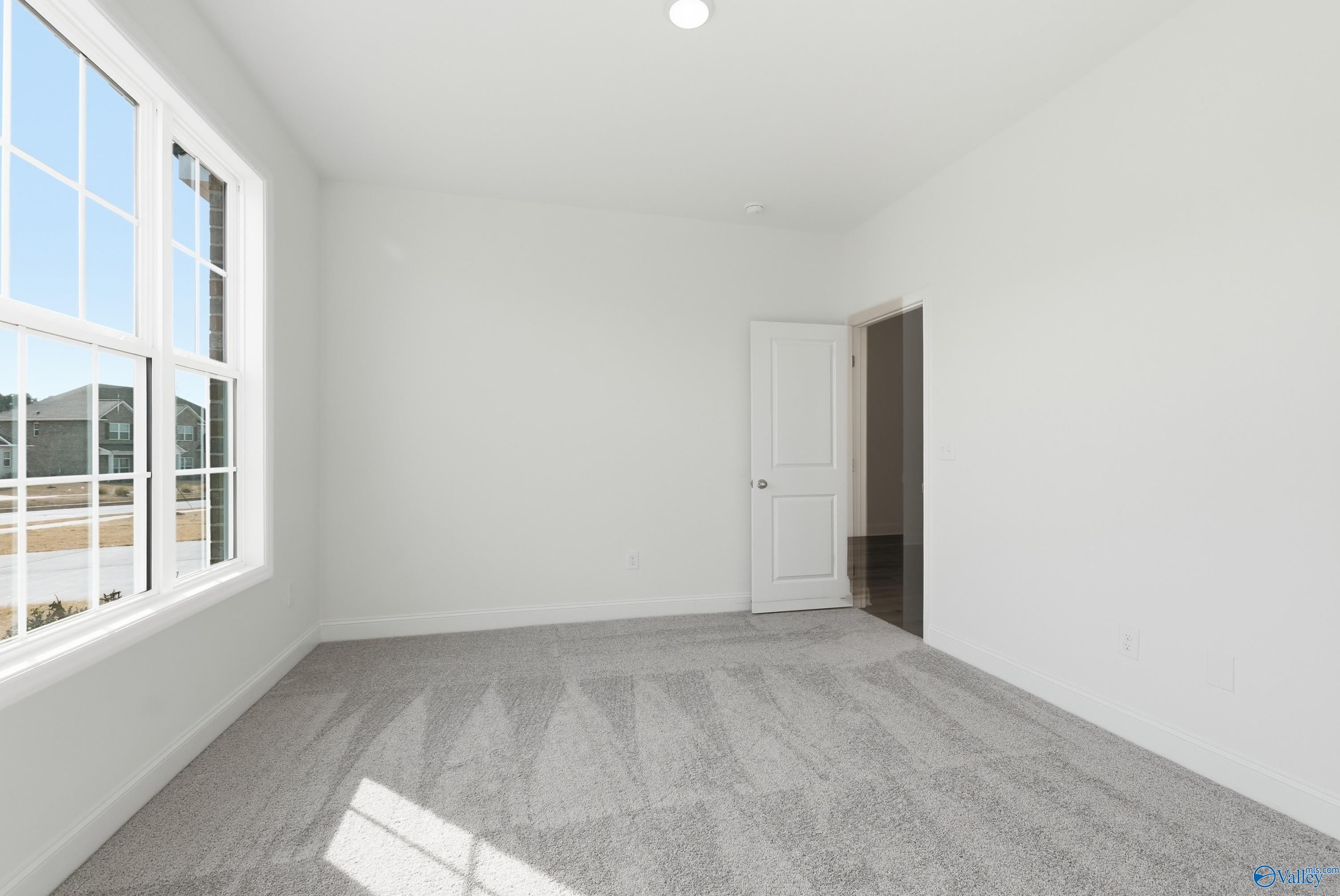 Bright sunlit bedroom with large windows, white walls, and neutral carpet in Davidson Homes Montgomery C, Harvest Alabama