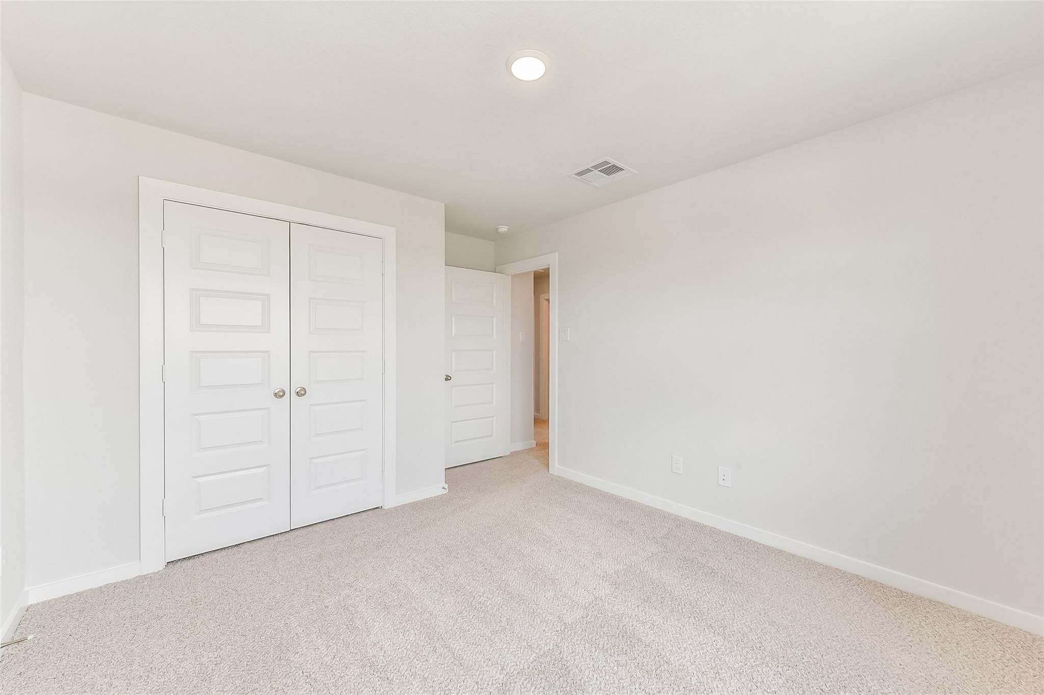 Bright secondary bedroom featuring walk-in closet, beige carpet, and white walls in Davidson Homes The Tierra C, Dayton, Texas