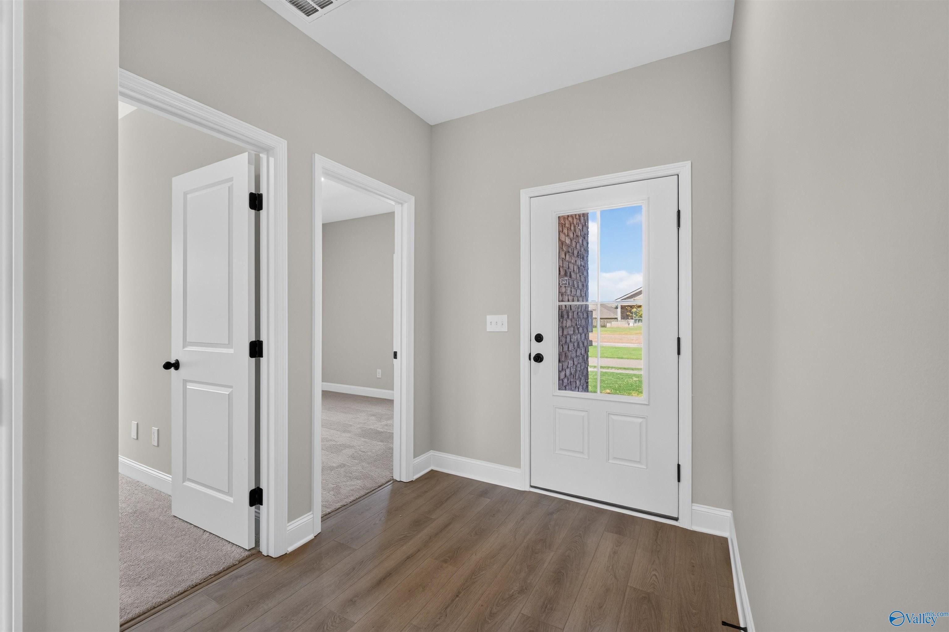 Bright foyer with glass-panel front door, hardwood floors, and white trim in Davidson Homes The Butler plan, Hazel Green, Alabama