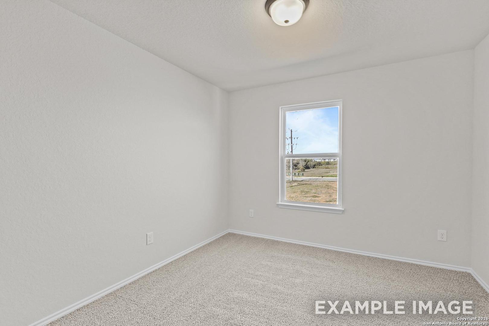 Bright empty bedroom with white walls, beige carpet, large window overlooking fields in The Trinity B by Davidson Homes, San Antonio