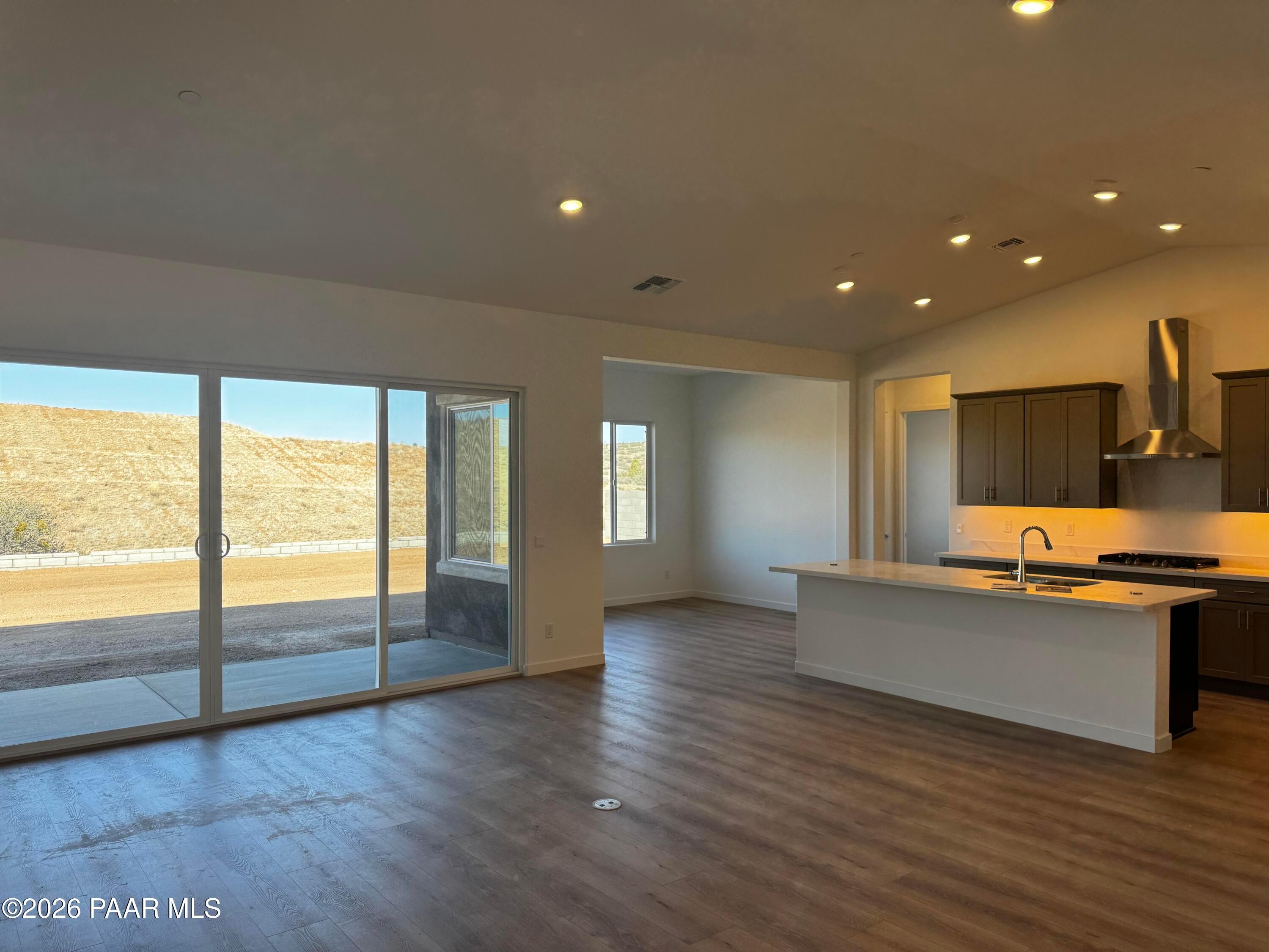 Open-concept great room featuring modern white kitchen island, stainless appliances, and sliding doors to desert landscape in The Blaze C, Prescott, Arizona