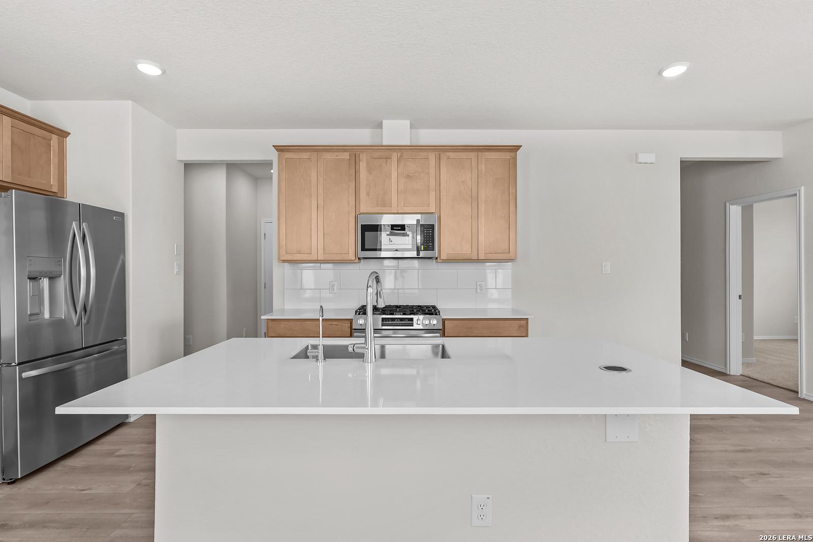 Modern kitchen with white quartz island, stainless steel appliances, and natural wood cabinets in The Gillian B floor plan.