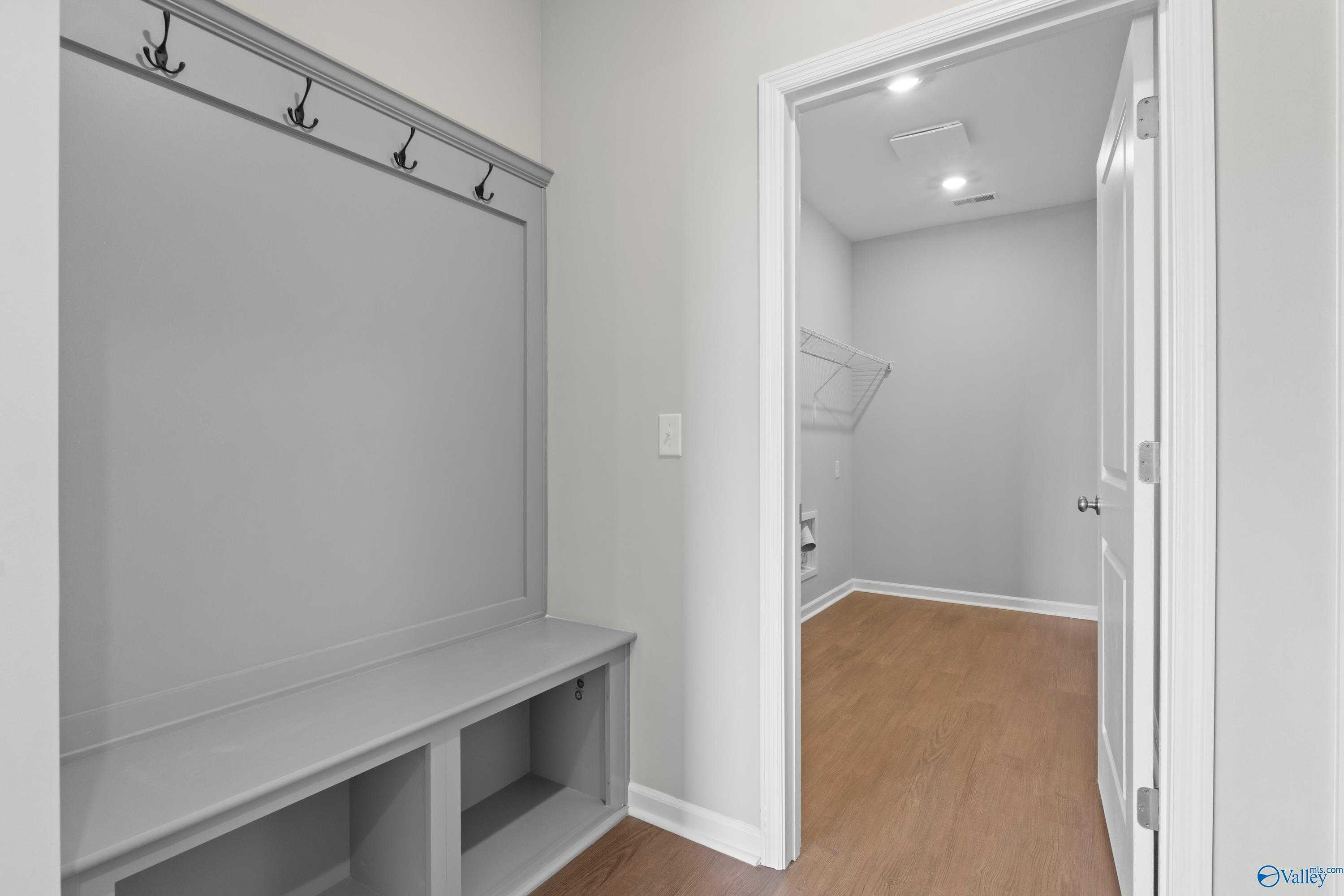 Functional mudroom with built-in gray bench, coat hooks, and adjacent laundry in Davidson Homes The Dorado, Athens, Alabama