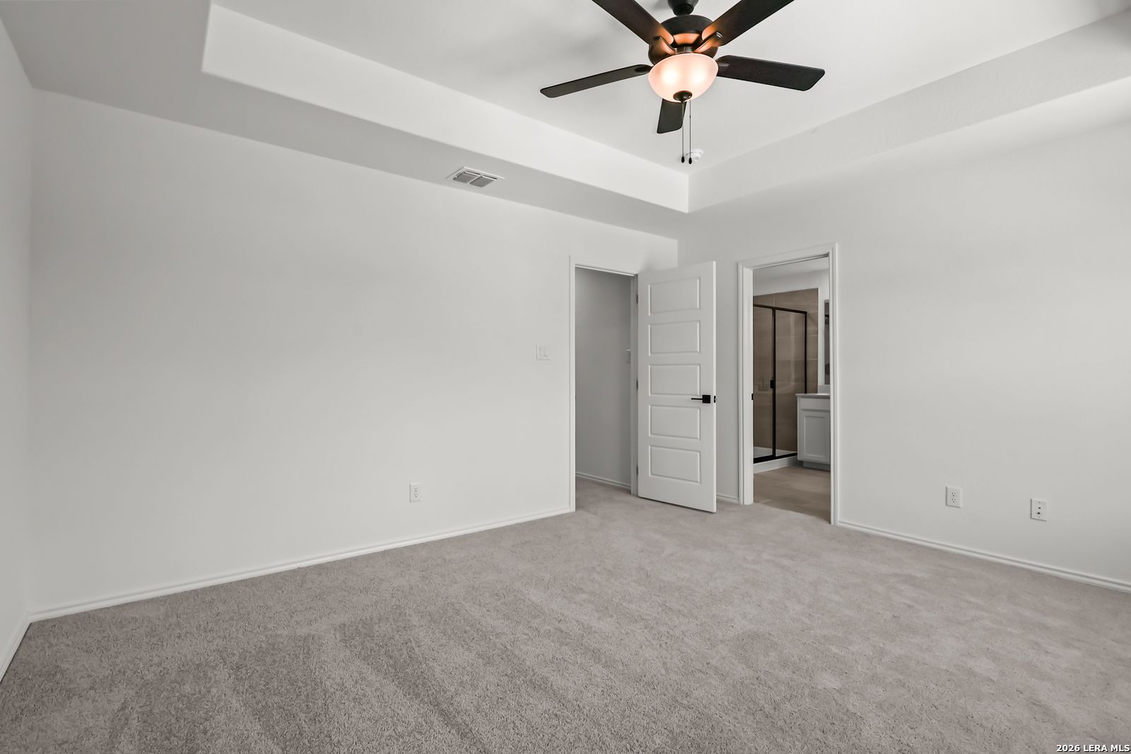 Bright bedroom with tray ceiling, ceiling fan, and en-suite bathroom in The Florence B floor plan, Meadows at Oak Creek.