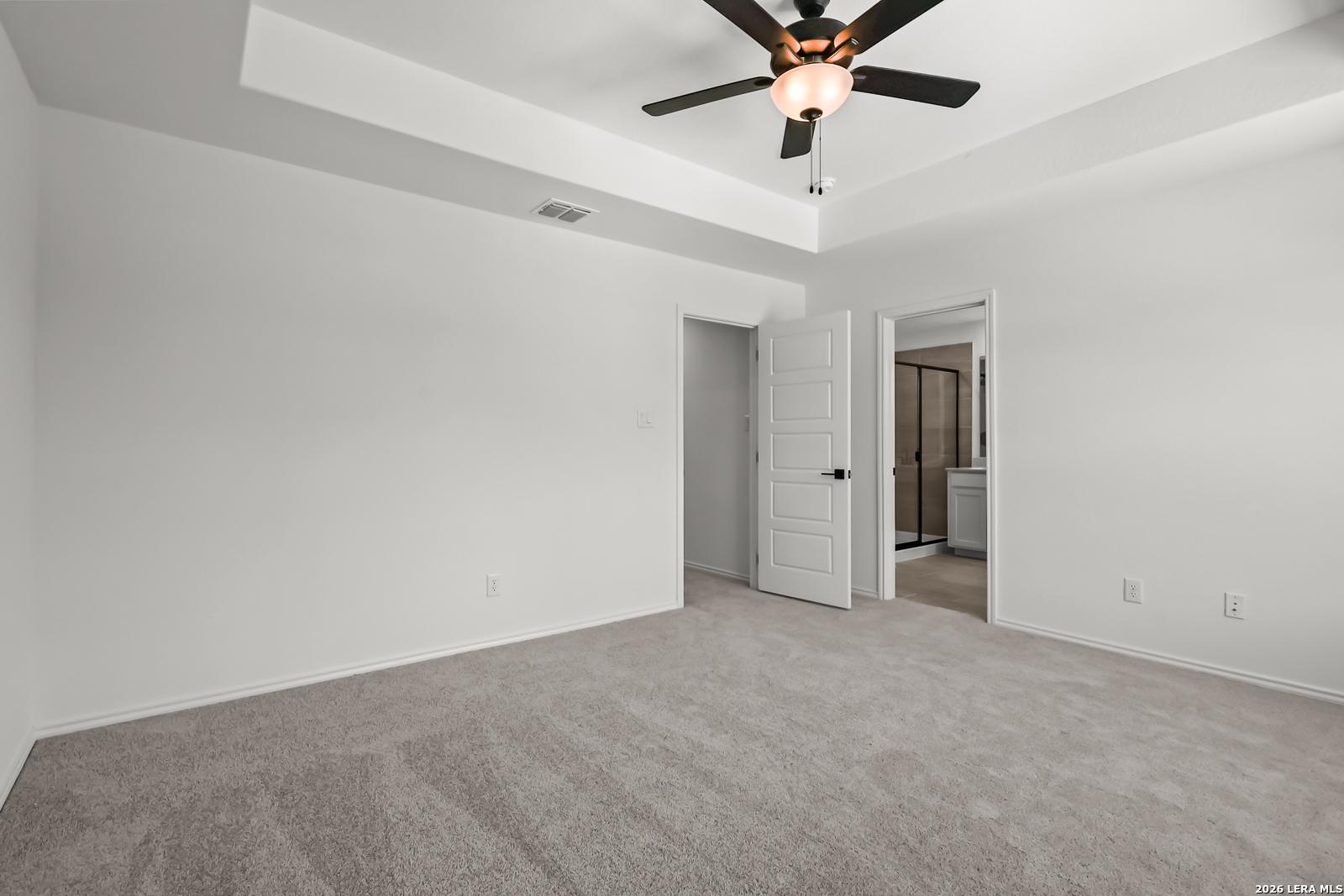 Bright bedroom with tray ceiling, ceiling fan, and en-suite bathroom in The Florence B floor plan, Meadows at Oak Creek.