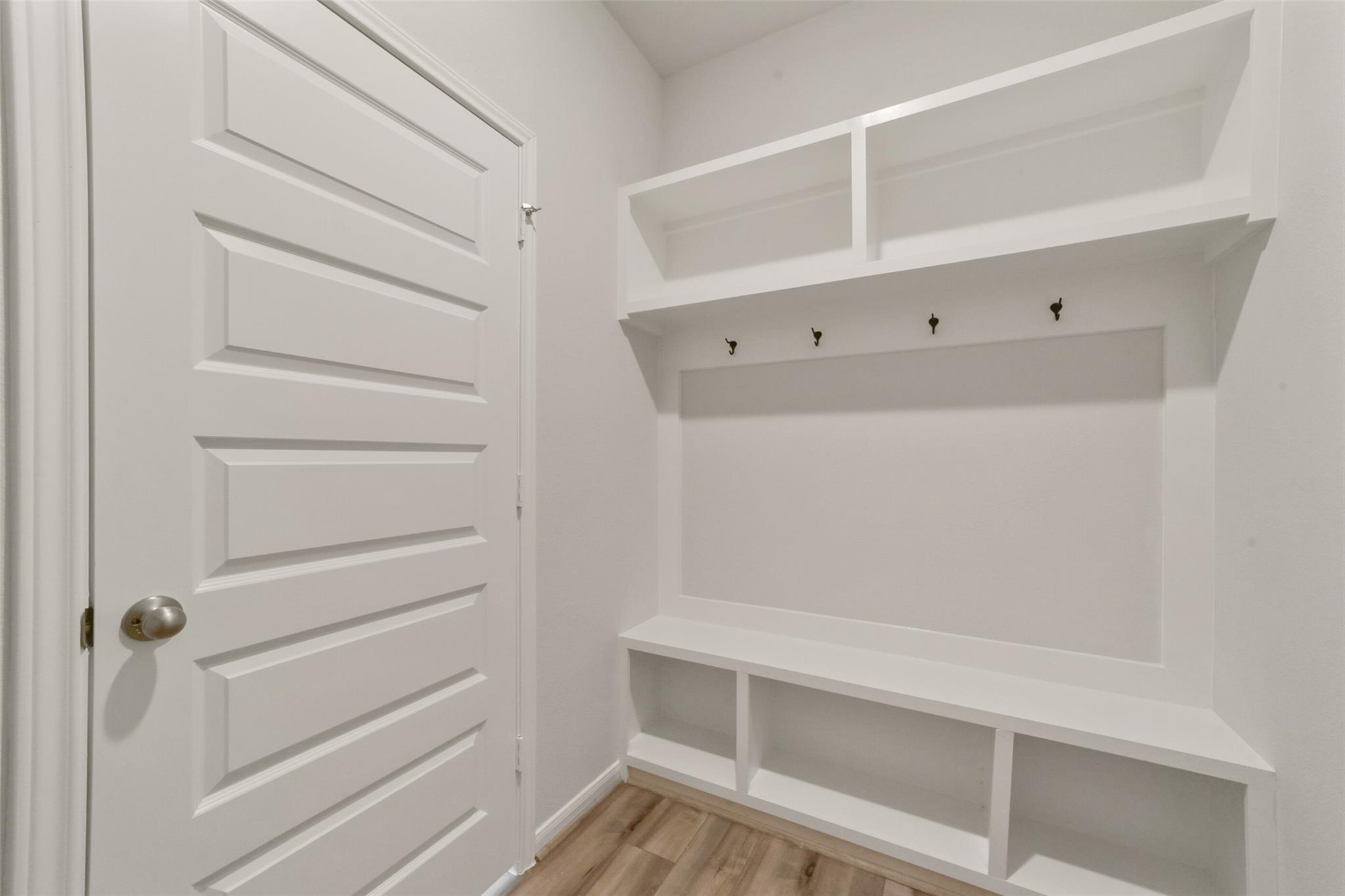 White mudroom featuring built-in bench, open shelves, and coat hooks in Davidson Homes San Marcos E, Beasley, Texas