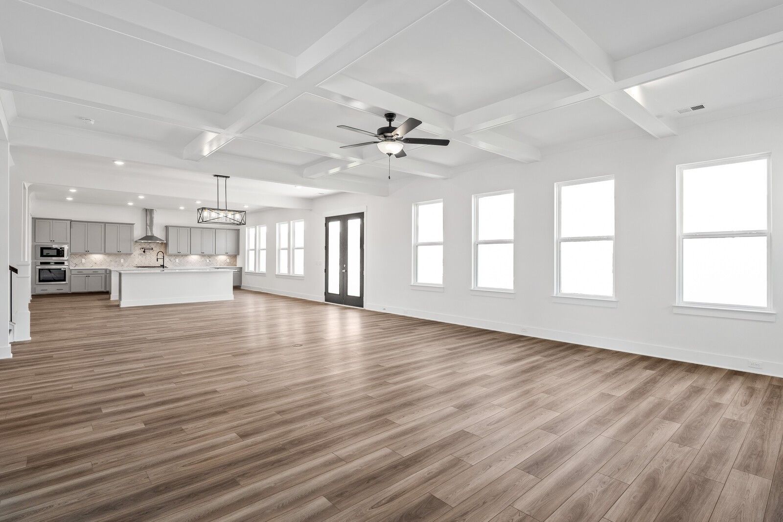 Open-concept living and kitchen with gray cabinets, white island, coffered ceiling, and large windows in The Alston A, Murfreesboro, TN