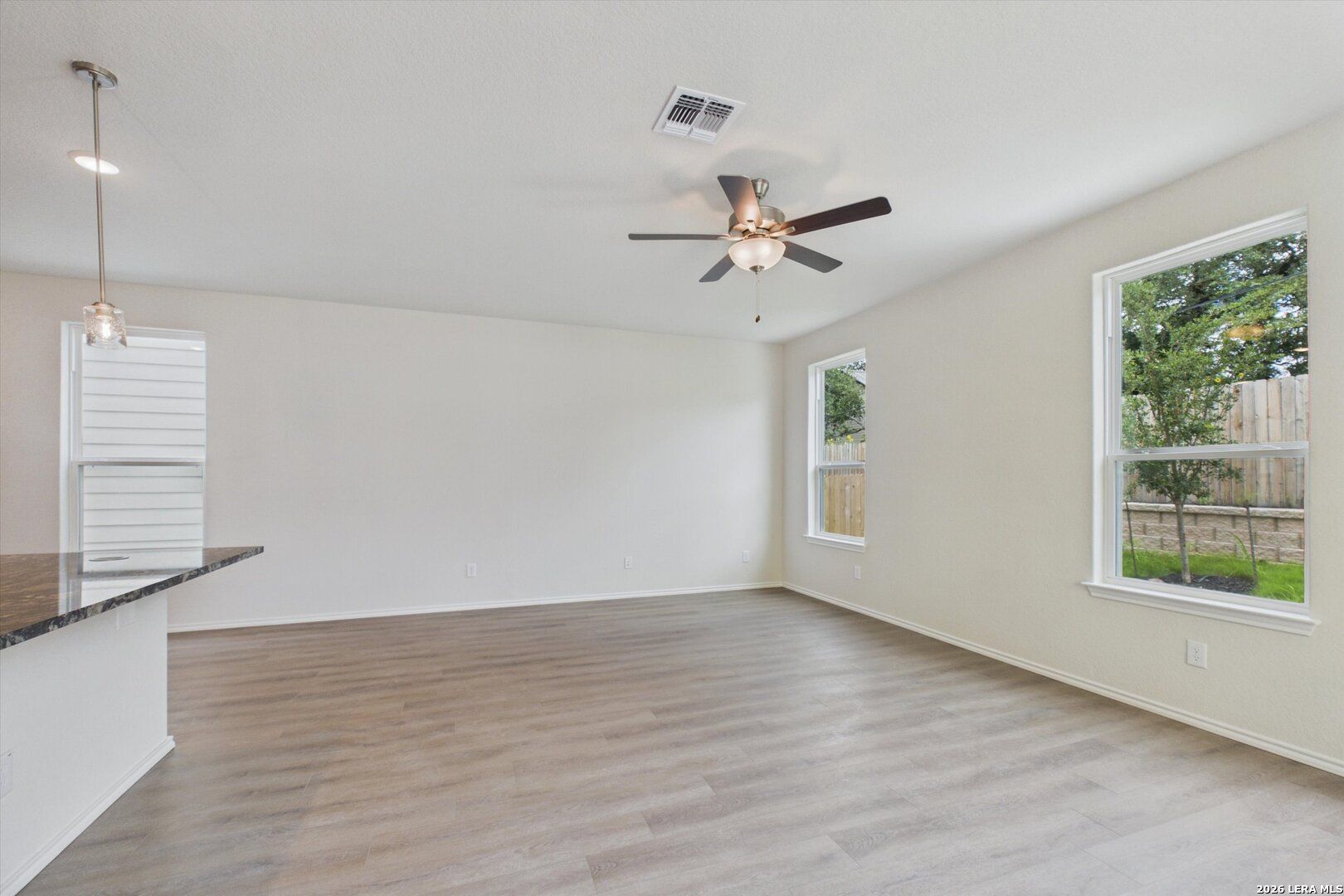 Bright open-concept living area with wood-style flooring in The Charlotte B floor plan at Meadows at Oak Creek, San Antonio.